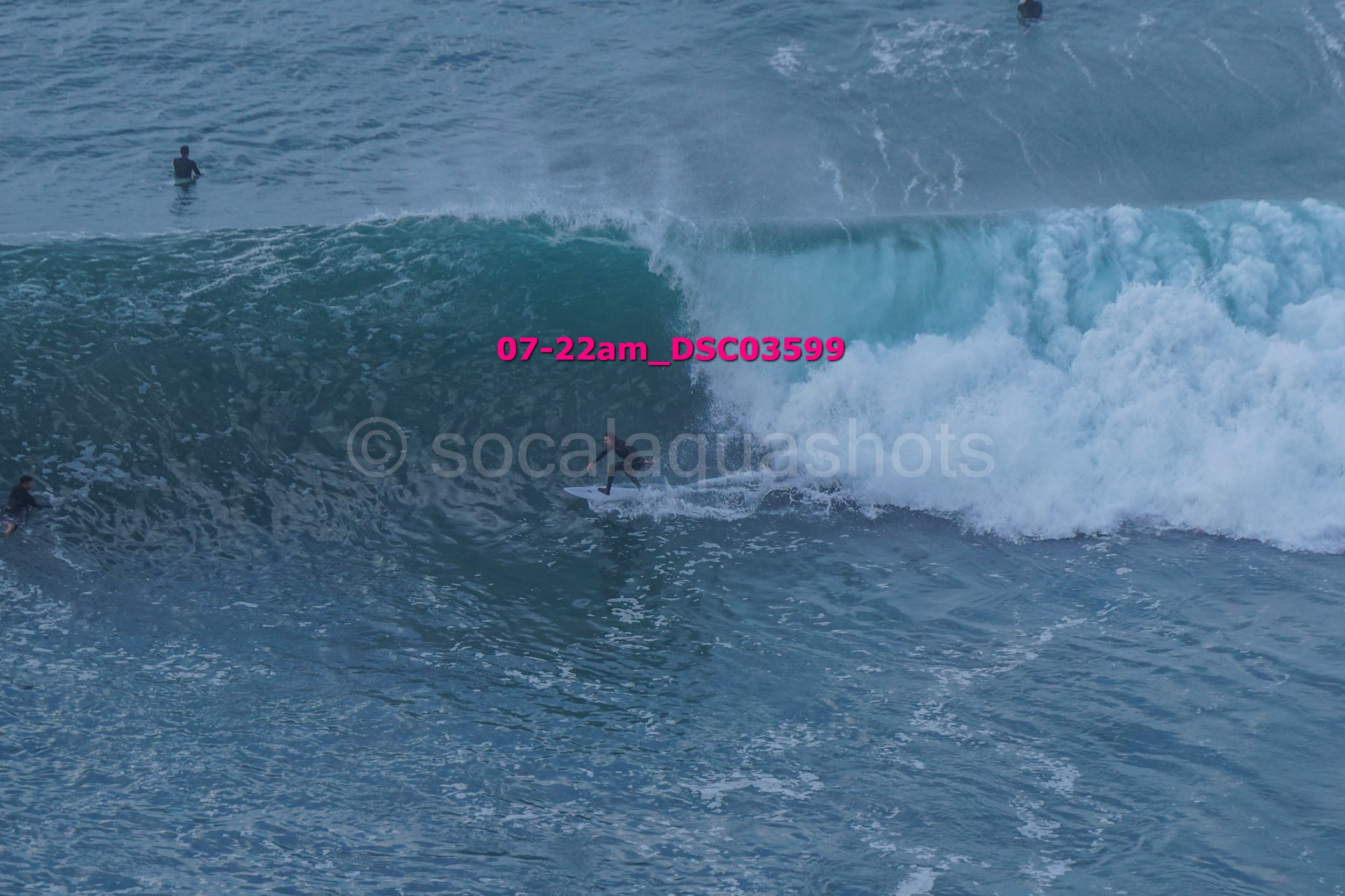 Surfer riding a large wave in the ocean with other surfers and a person swimming in the background.