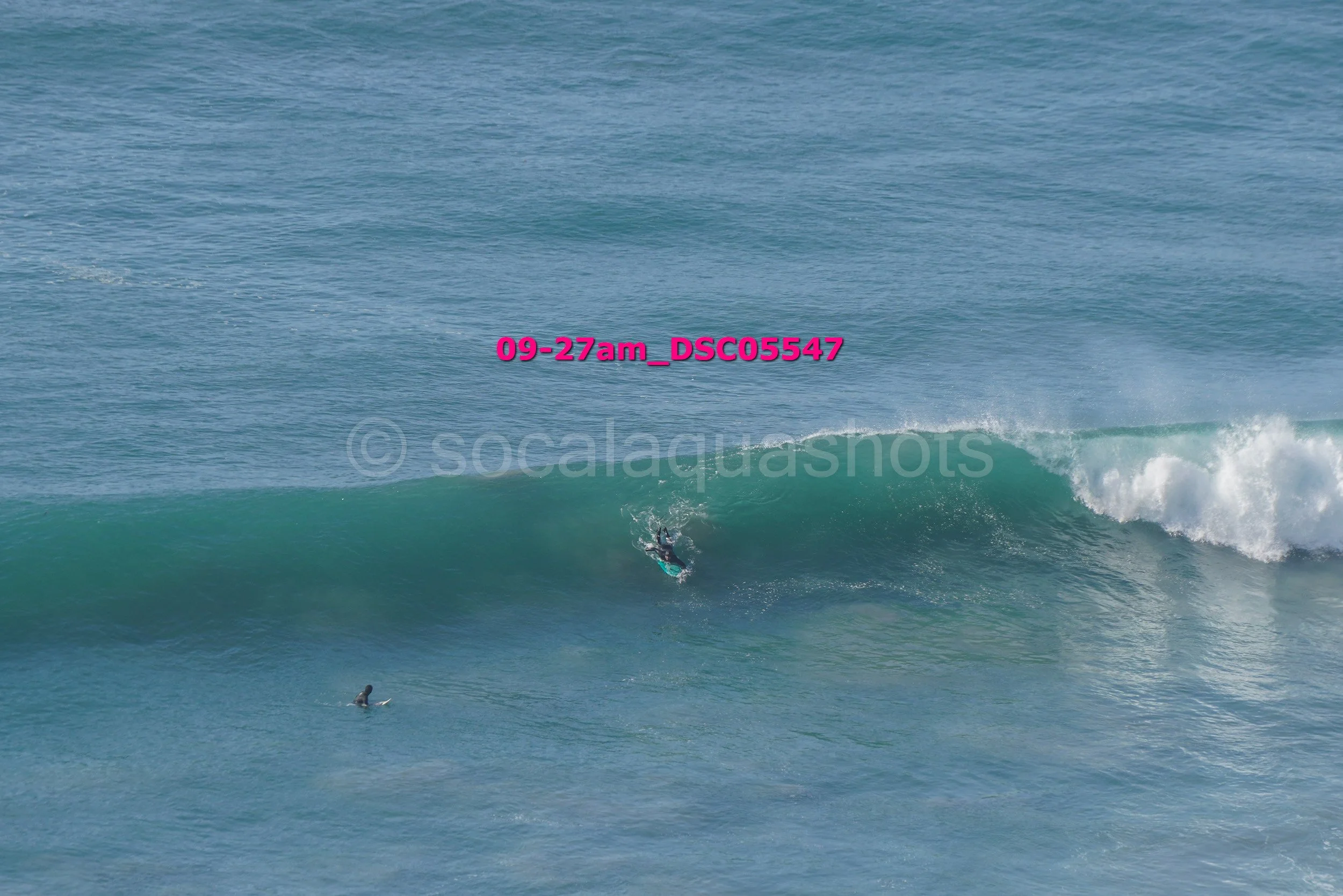 A person surfing on a large wave in the ocean with another surfer floating nearby