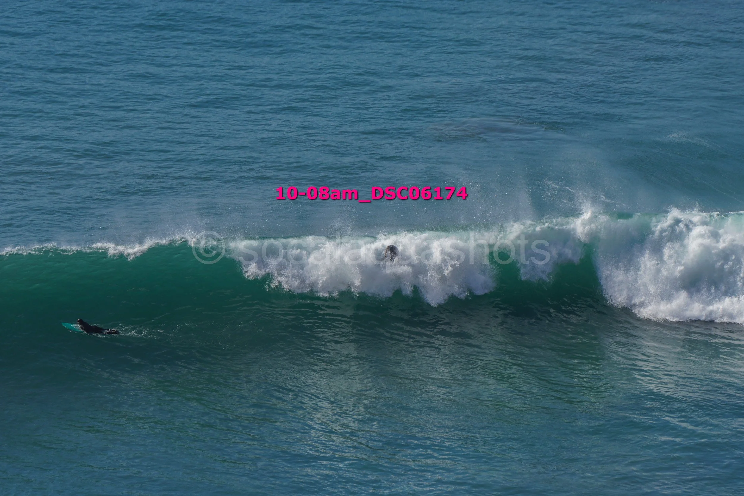 A person surfing on a large wave in the ocean, with another person swimming nearby.