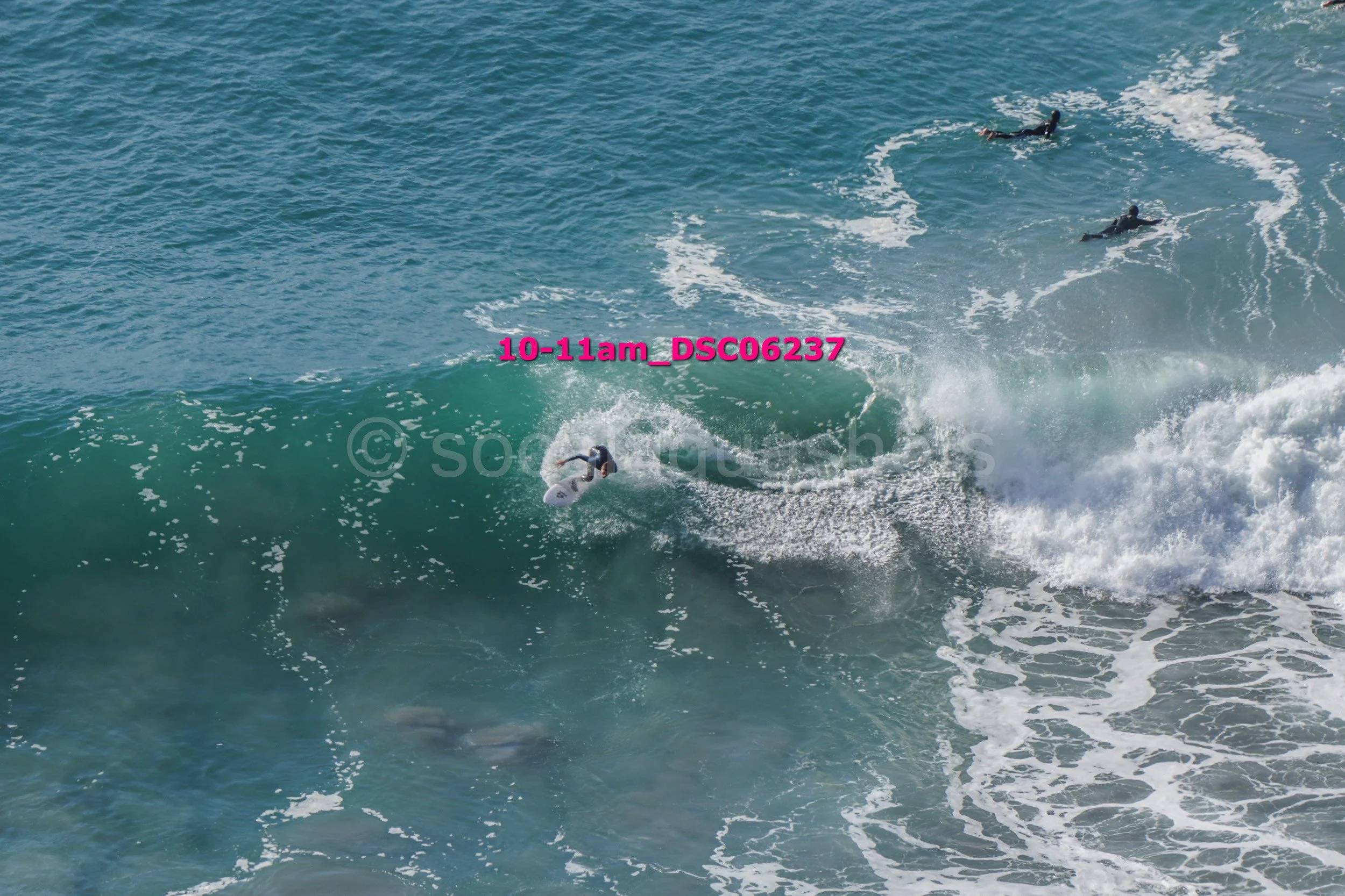 A surfer riding a wave with two other surfers in the water nearby.