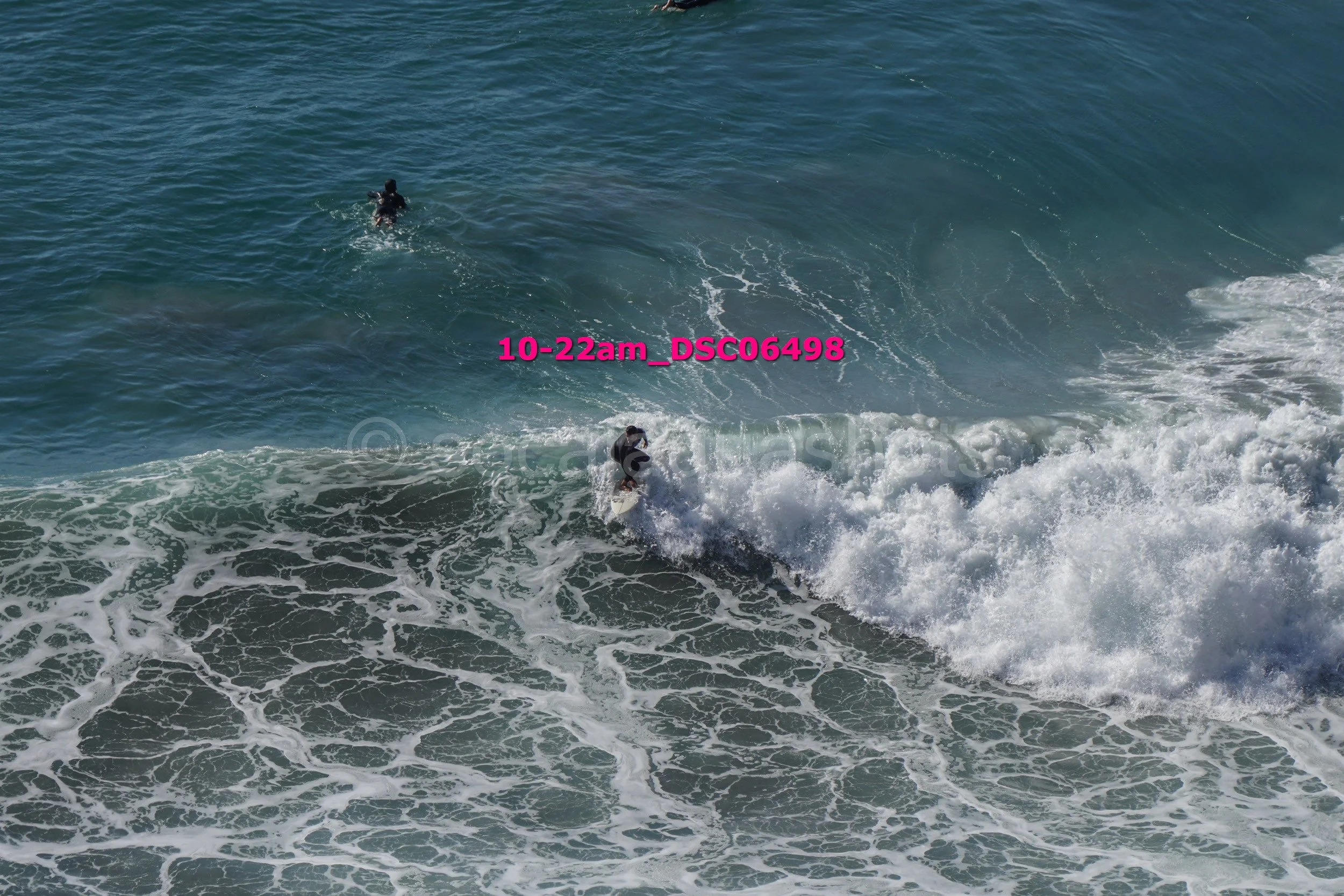 A person surfing waves in the ocean with another individual swimming nearby.