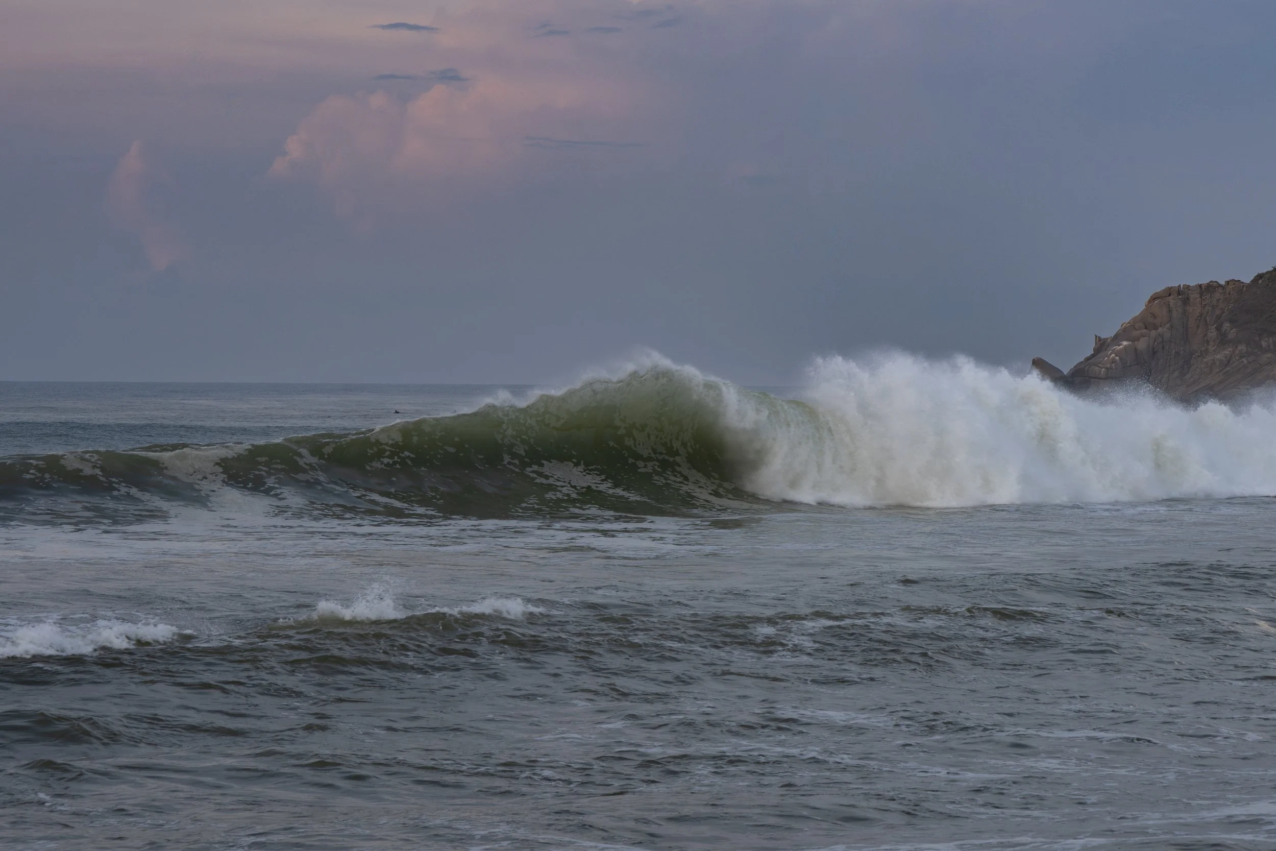 Ocean waves crashing near rocks under a cloudy sky.