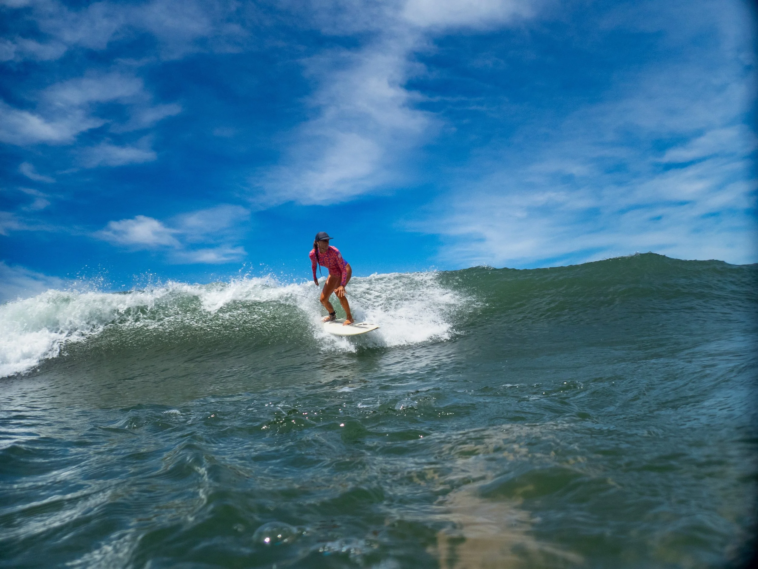A woman surfing on a wave under a partly cloudy blue sky.