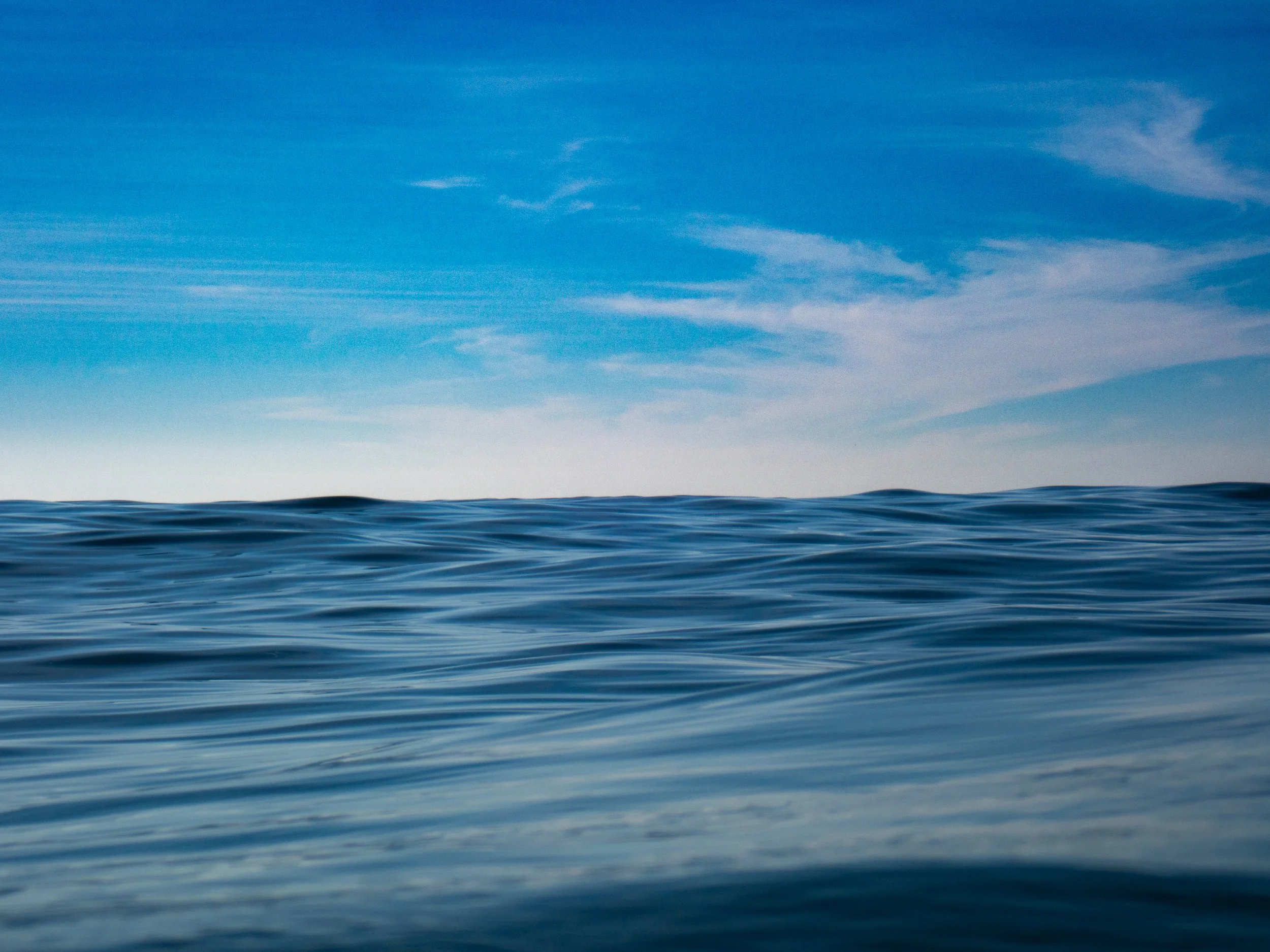 Open ocean with gentle waves under a blue sky with light clouds.
