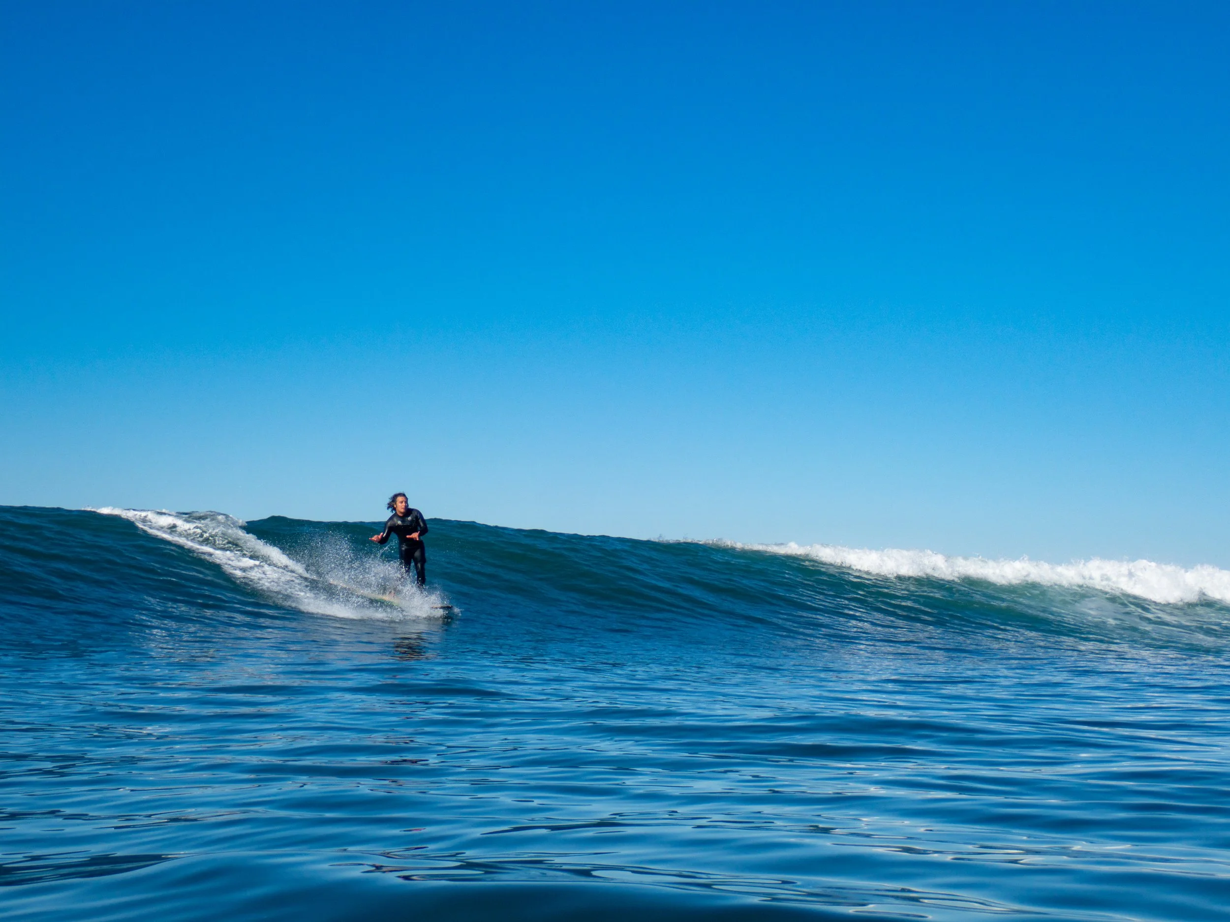 A person surfing on an ocean wave under a clear blue sky.
