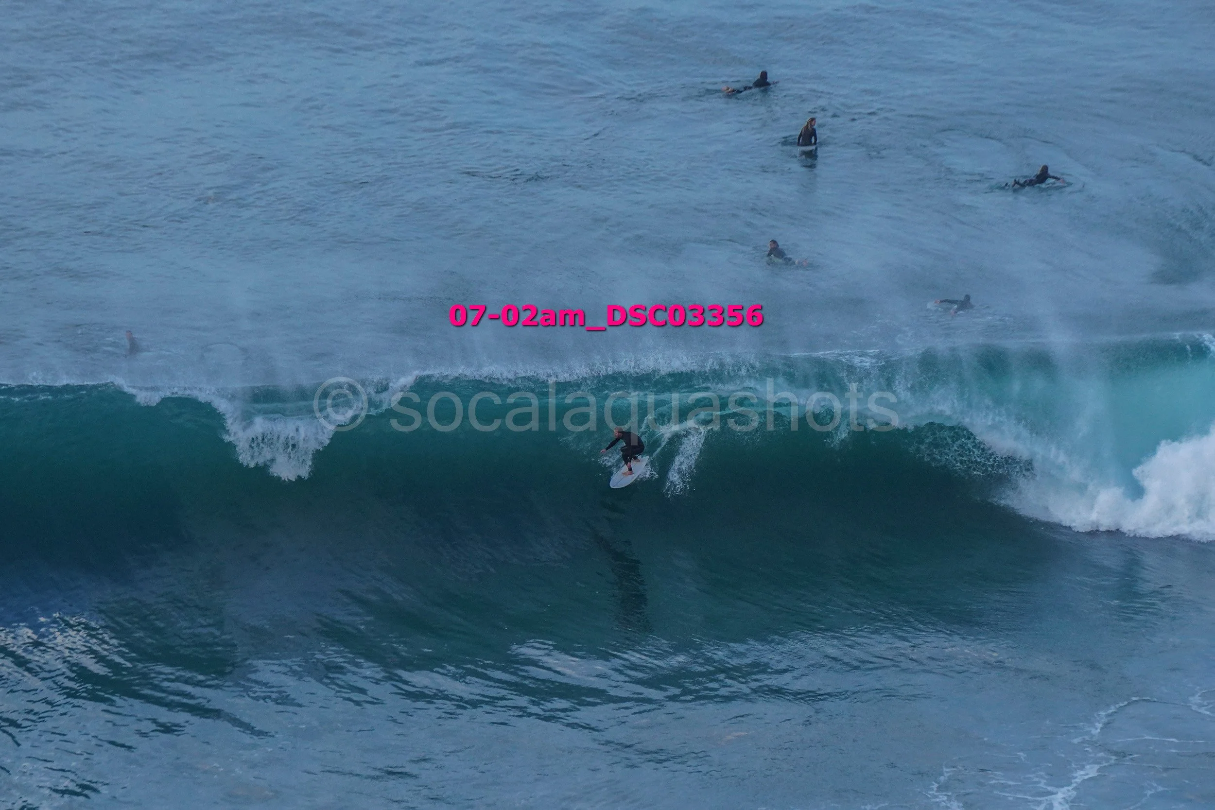 Surfer riding a wave with several people swimming or surfing in the background in the ocean.