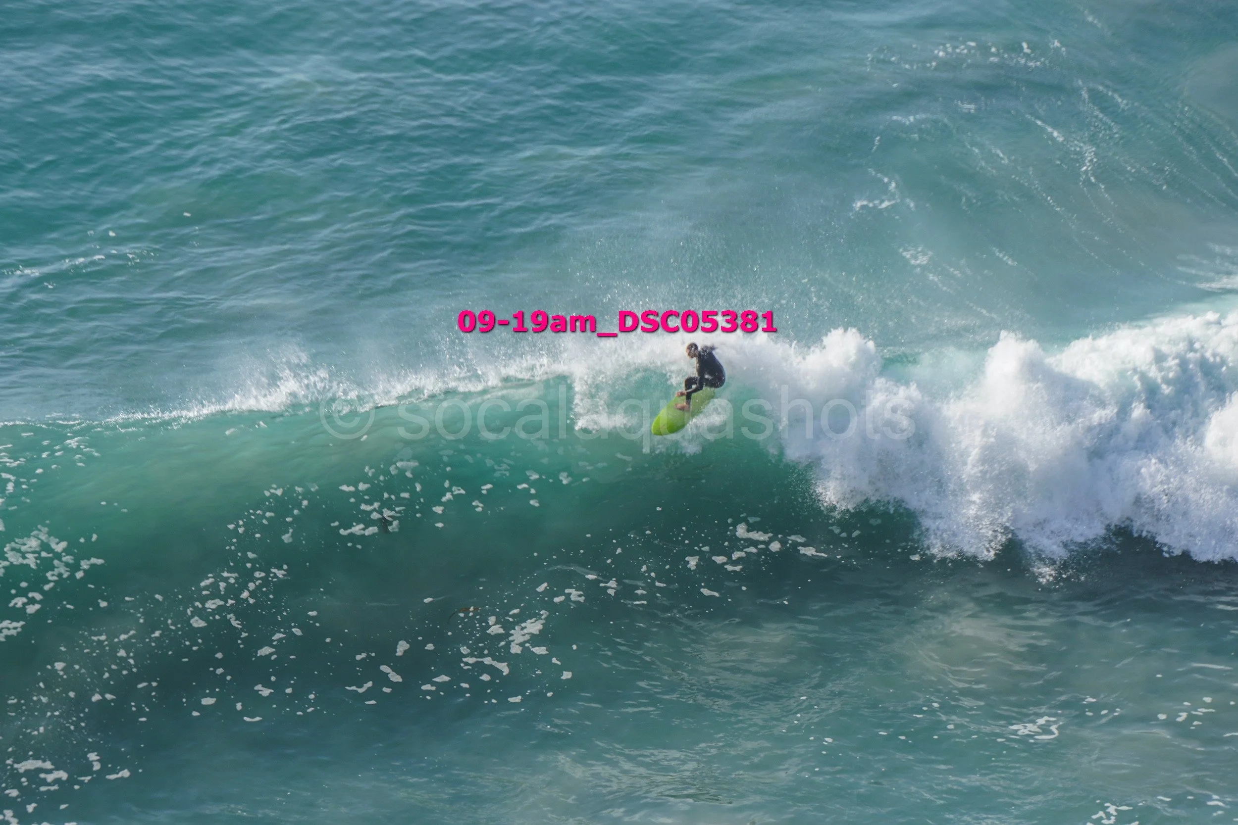 A person in a wetsuit surfing on a green surfboard riding a large ocean wave during daylight.