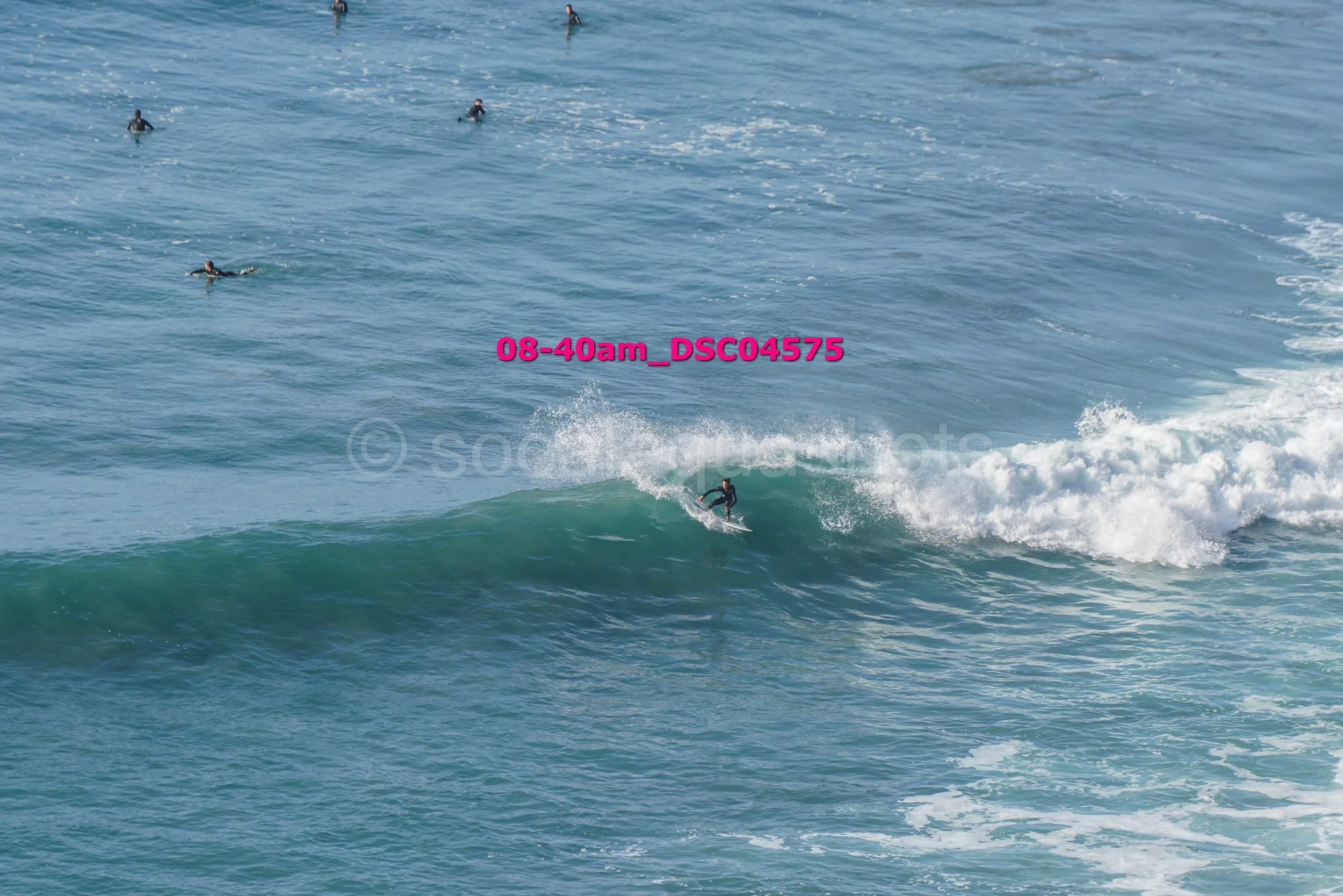 A person surfing on a wave with several other surfers floating in the water in the background.