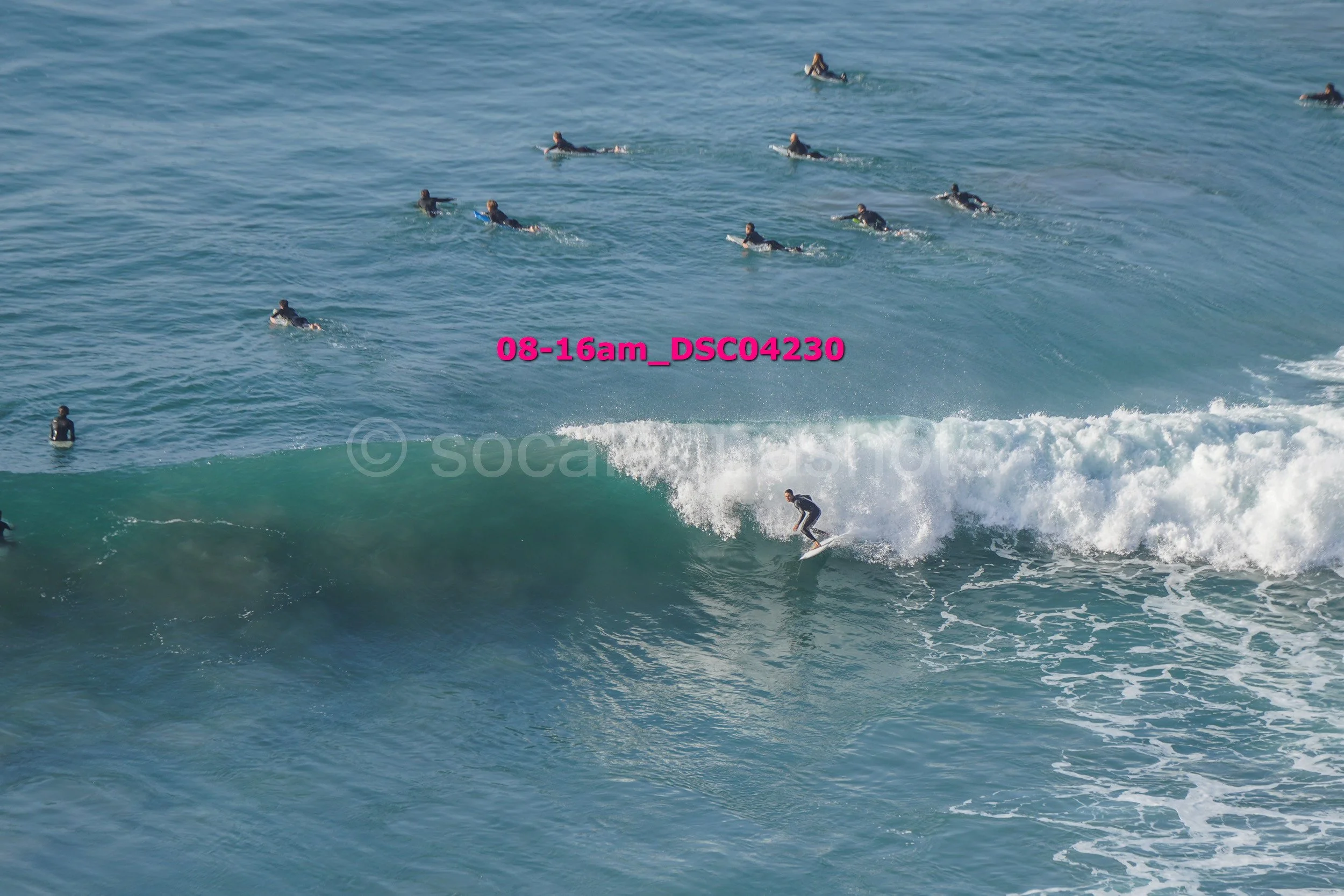 A person surfing on a wave with many surfers in the water around them.