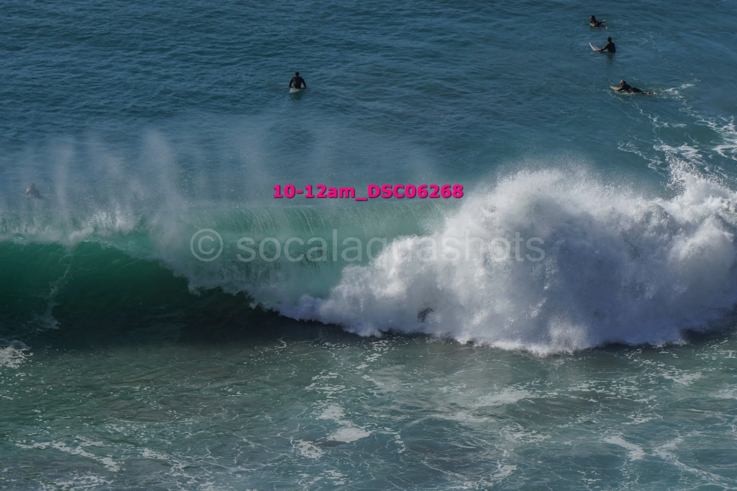 Surfing at the beach with several surfers riding a large wave in the ocean.