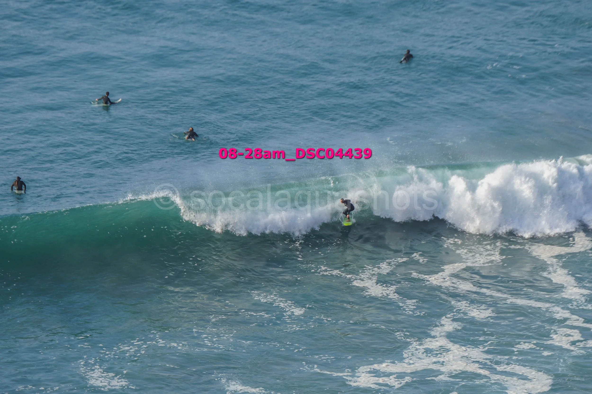 A person surfing on a wave in the ocean with several people in the water nearby.