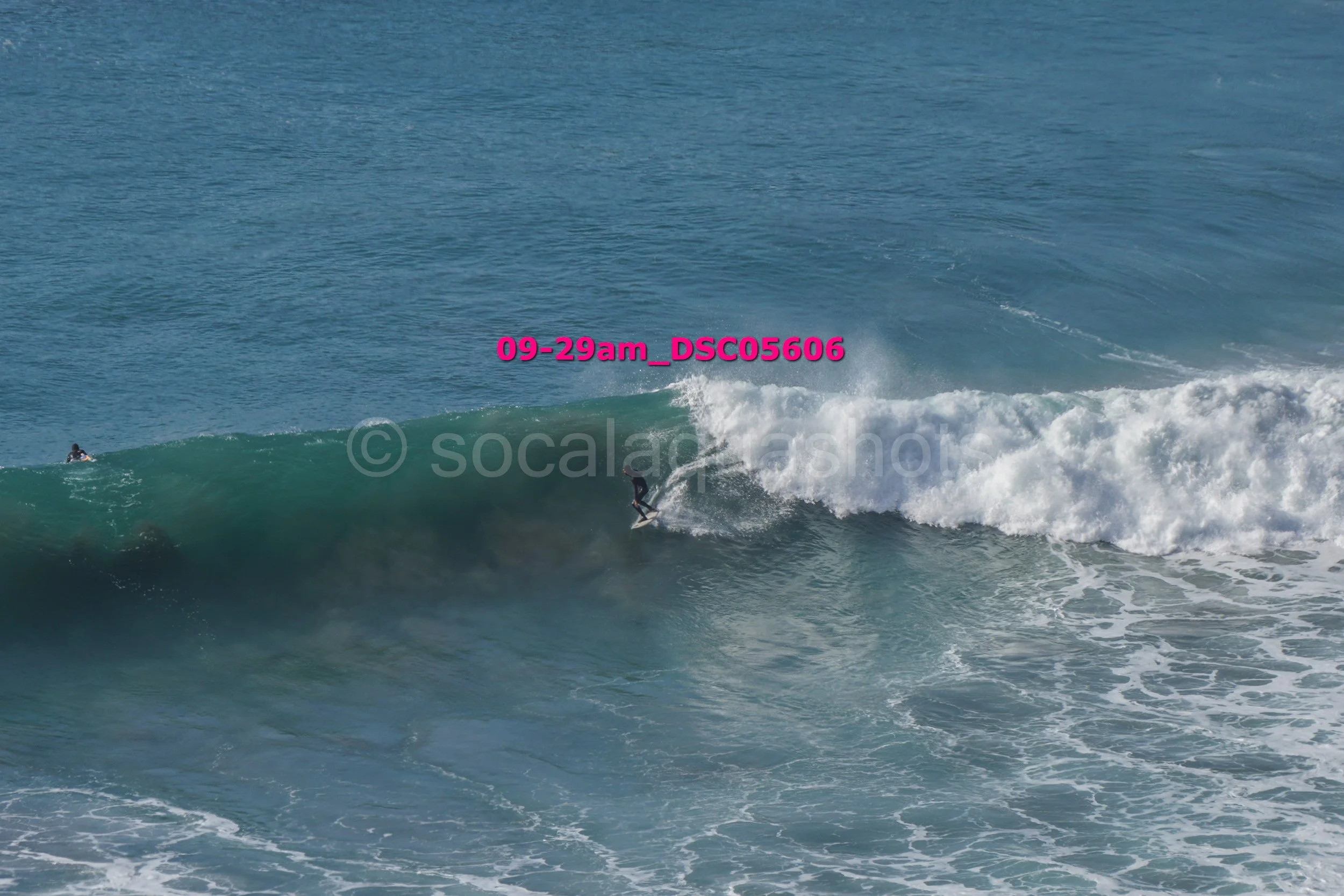 A person surfing on a large ocean wave with another individual in the water nearby.