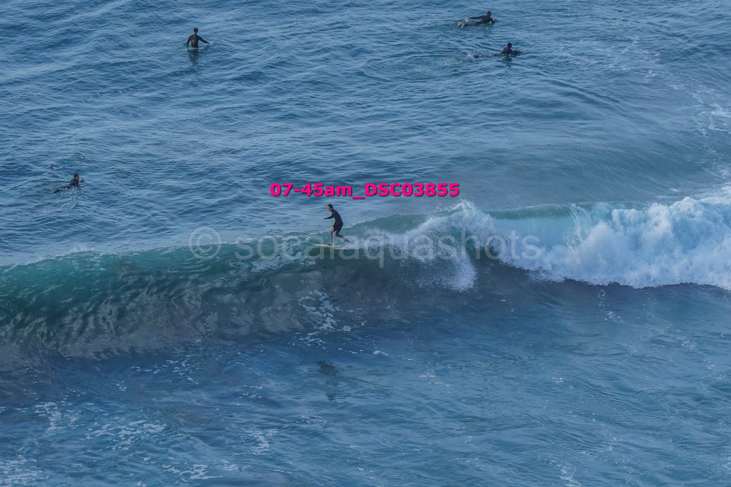 A person surfing on a wave in the ocean surrounded by several other swimmers or surfers.