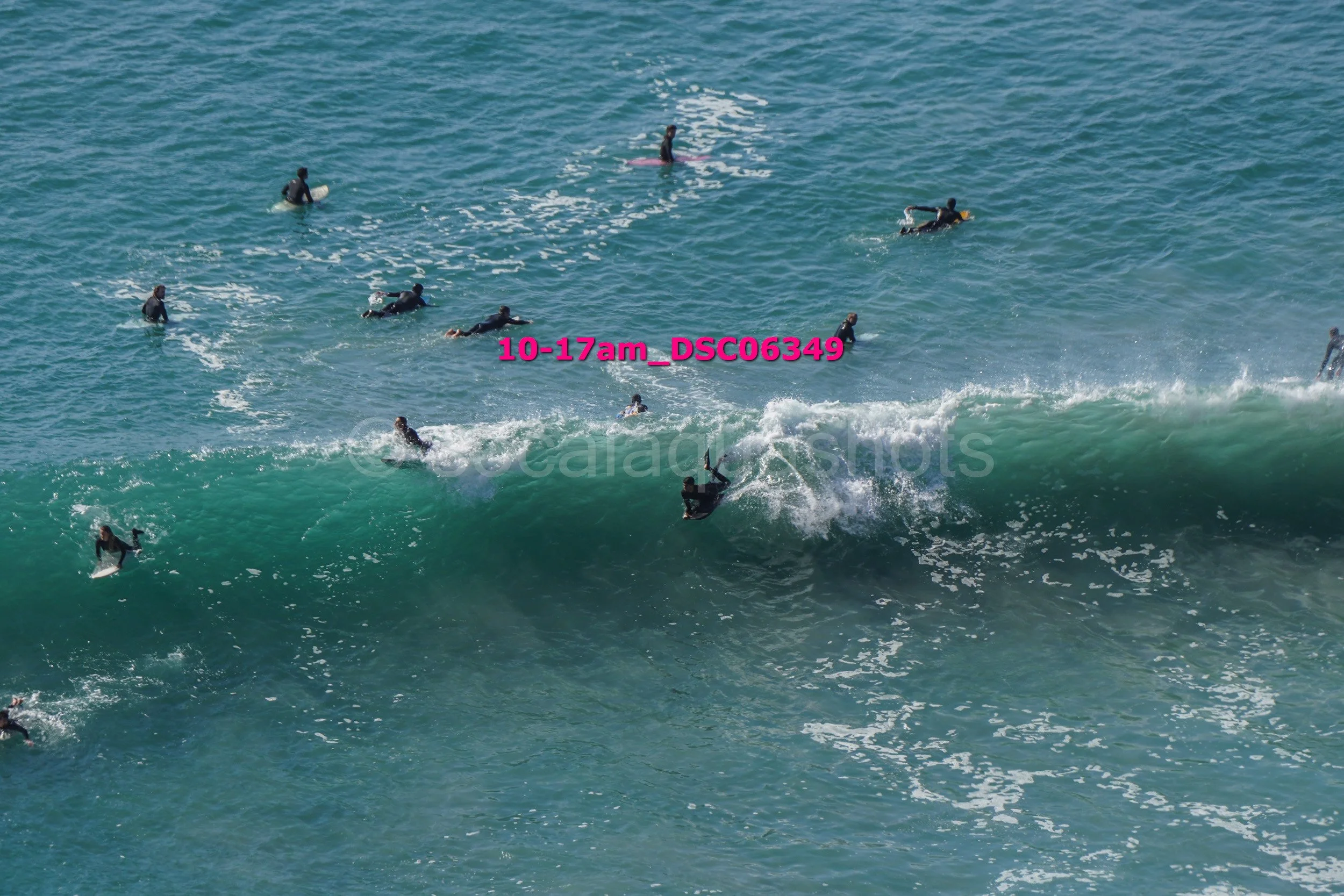 Group of surfers in wetsuits riding and waiting for waves in the ocean.