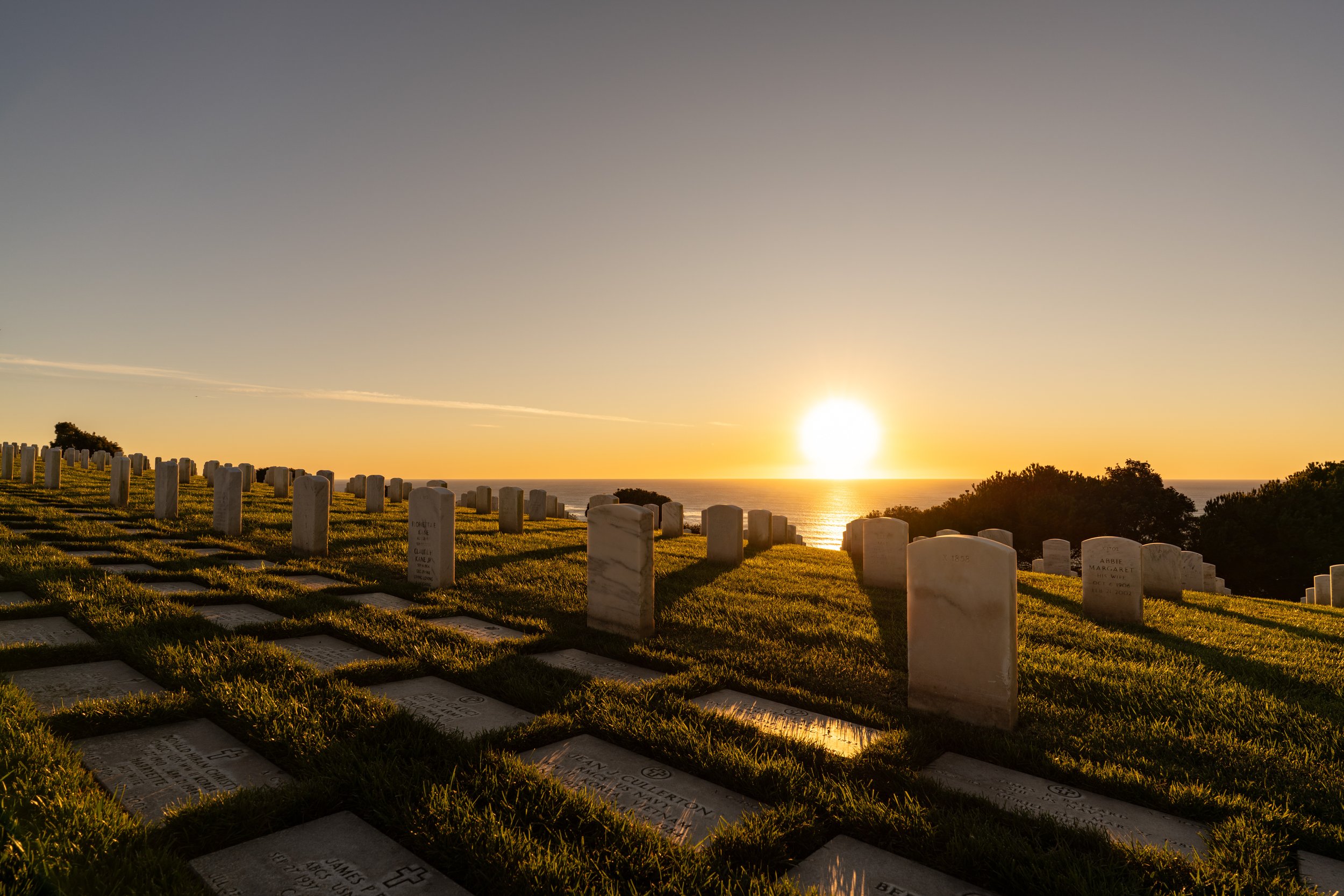 A cemetery on a hillside with white gravestones and a view of the ocean at sunset.
