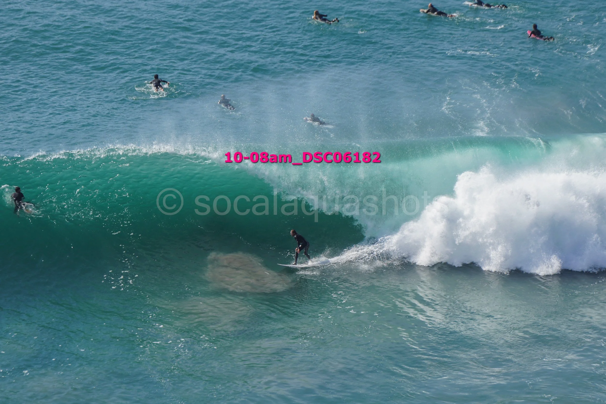 A person surfing on a wave with several other surfers in the water around them.