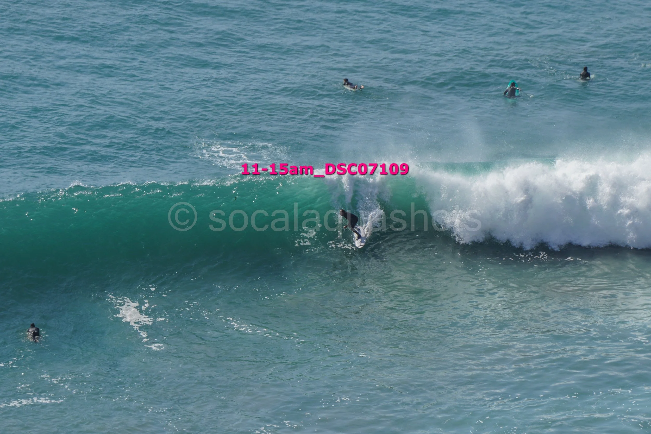 Person surfing on a wave at the beach with several other surfers in the water