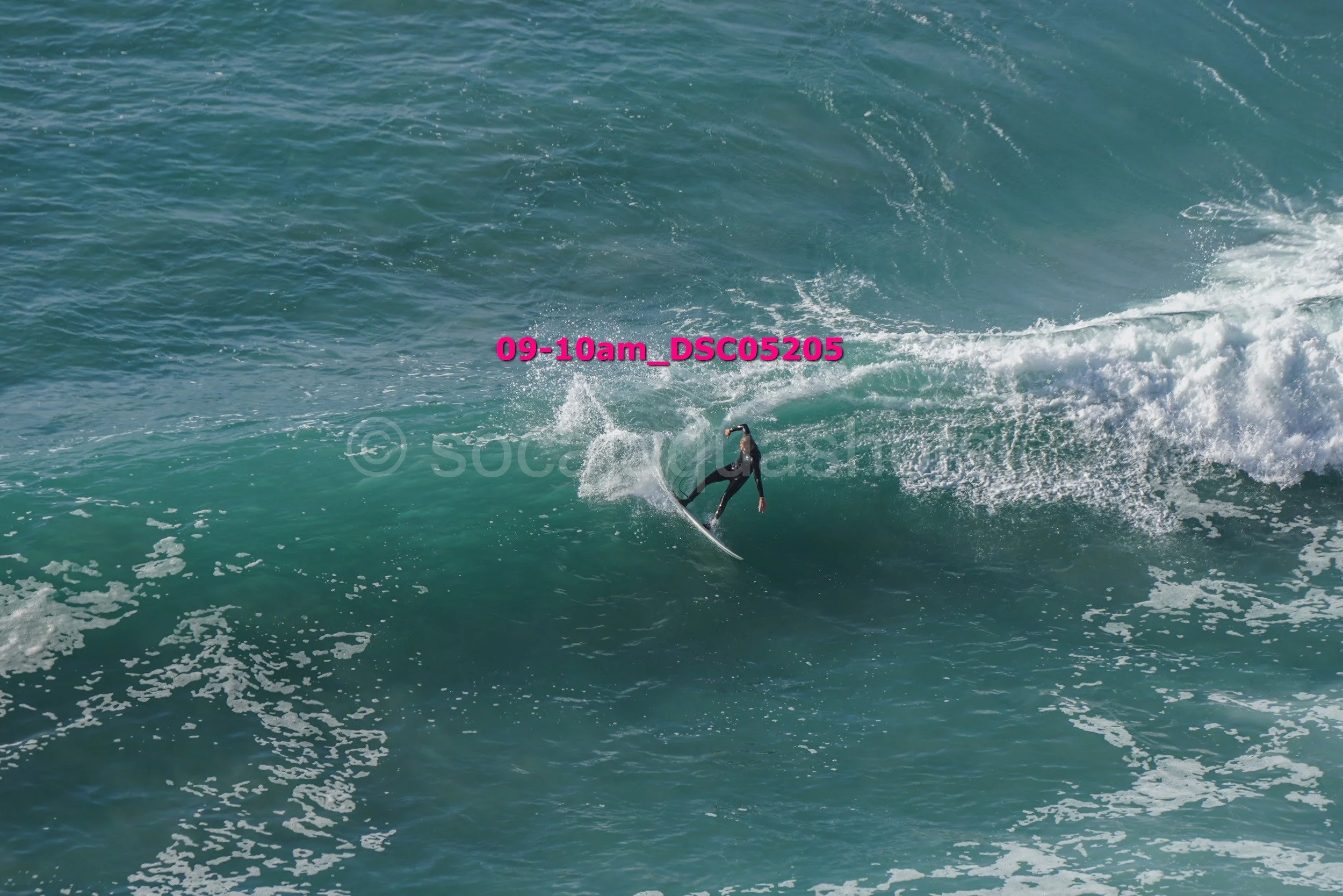 Surfer riding a wave in the ocean with some white foam and spray, in a wetsuit, during the daytime.