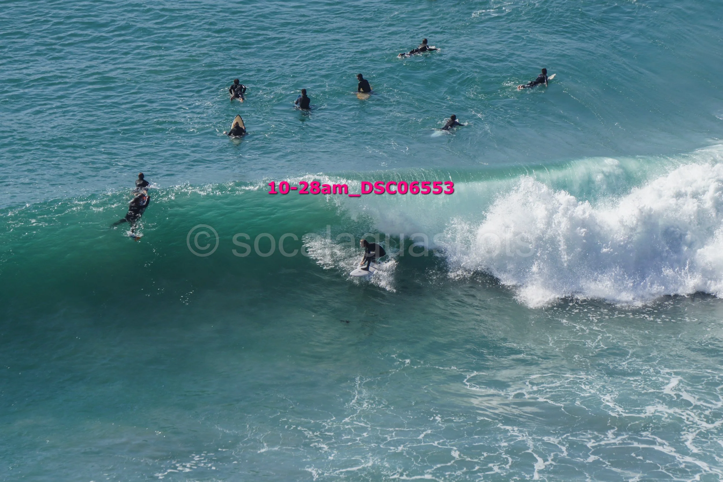 A group of people surfing in the ocean, some riding a wave and others waiting in the water.