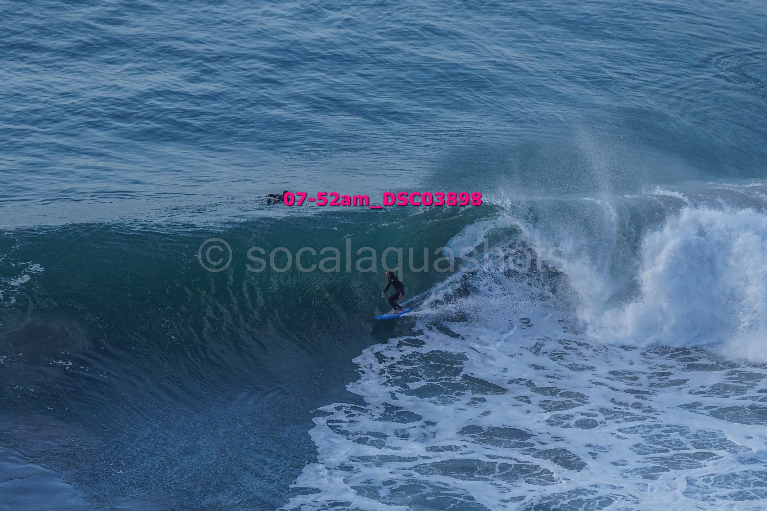 A person surfing on a large ocean wave with a smaller wave in the background.