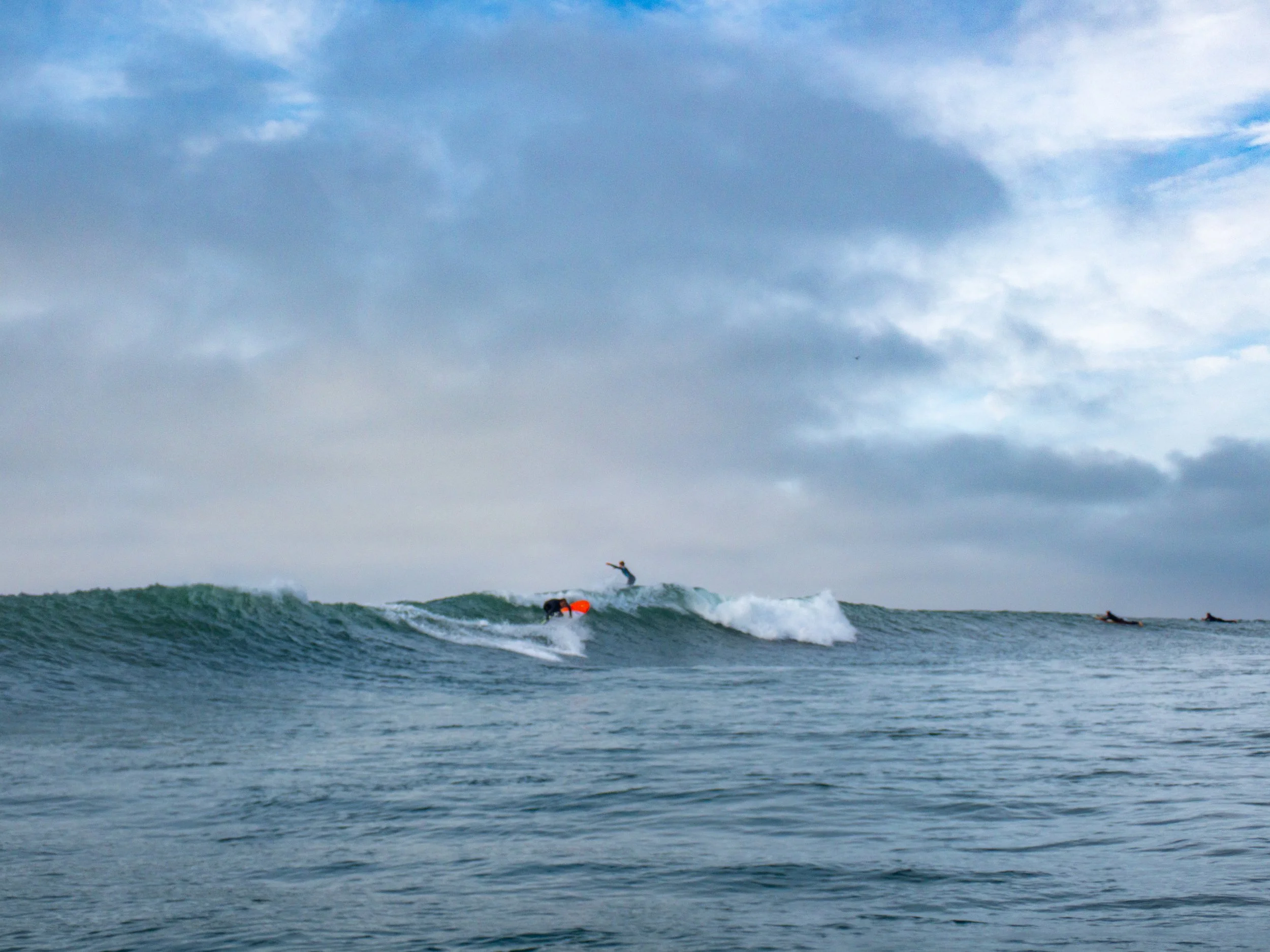 People surfing on ocean waves under cloudy sky.