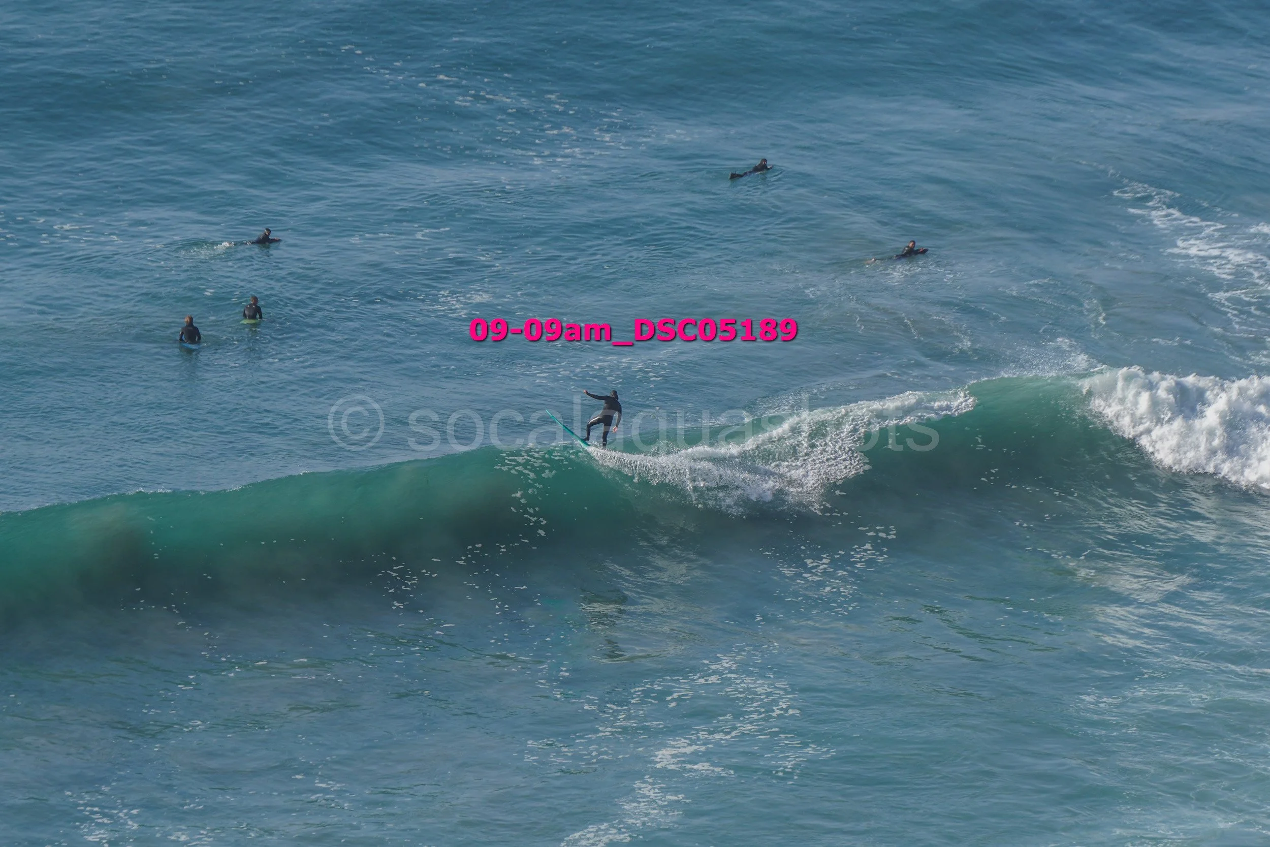 Surfer riding a wave in the ocean with several other surfers in the water nearby.