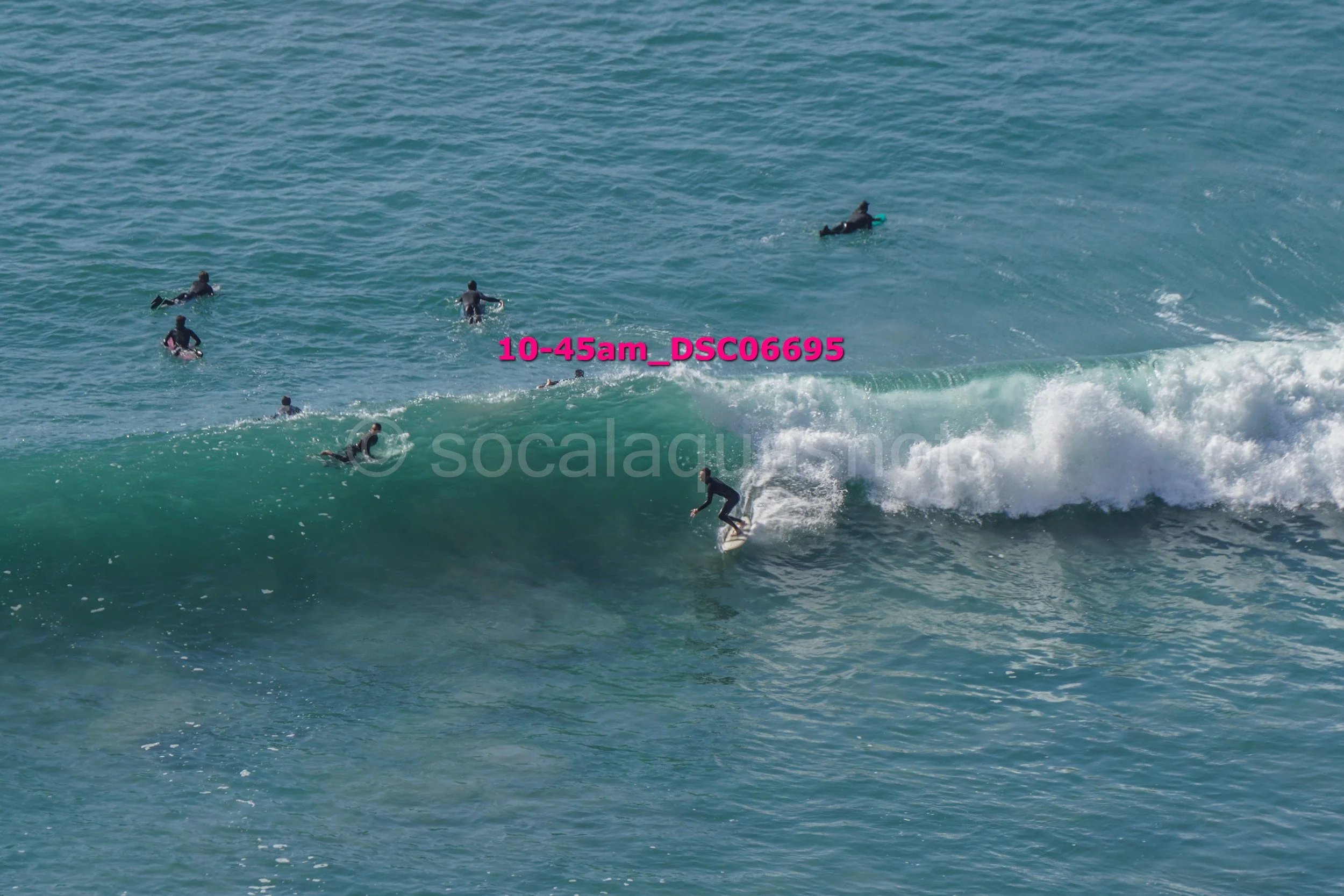 Surfer riding a wave with several surfers floating in the ocean nearby.