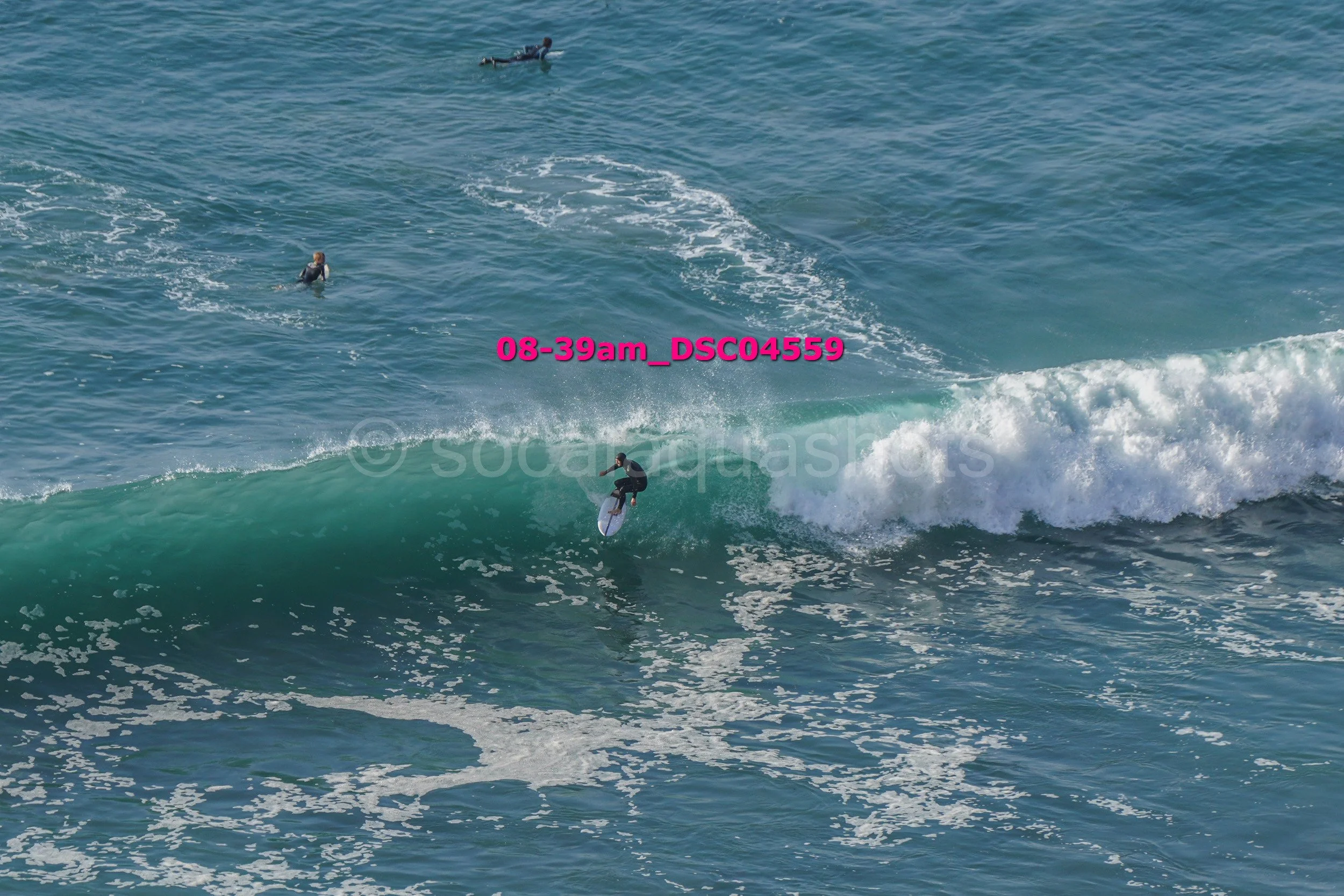 Surfer riding a wave in the ocean with three other surfers in the water, visible in the background.