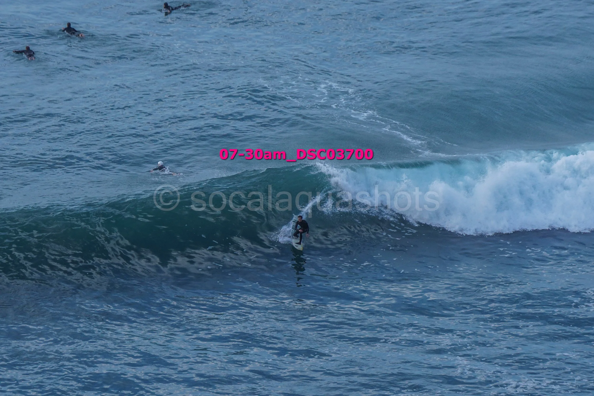 A person surfing on a wave with several other surfers in the water nearby.