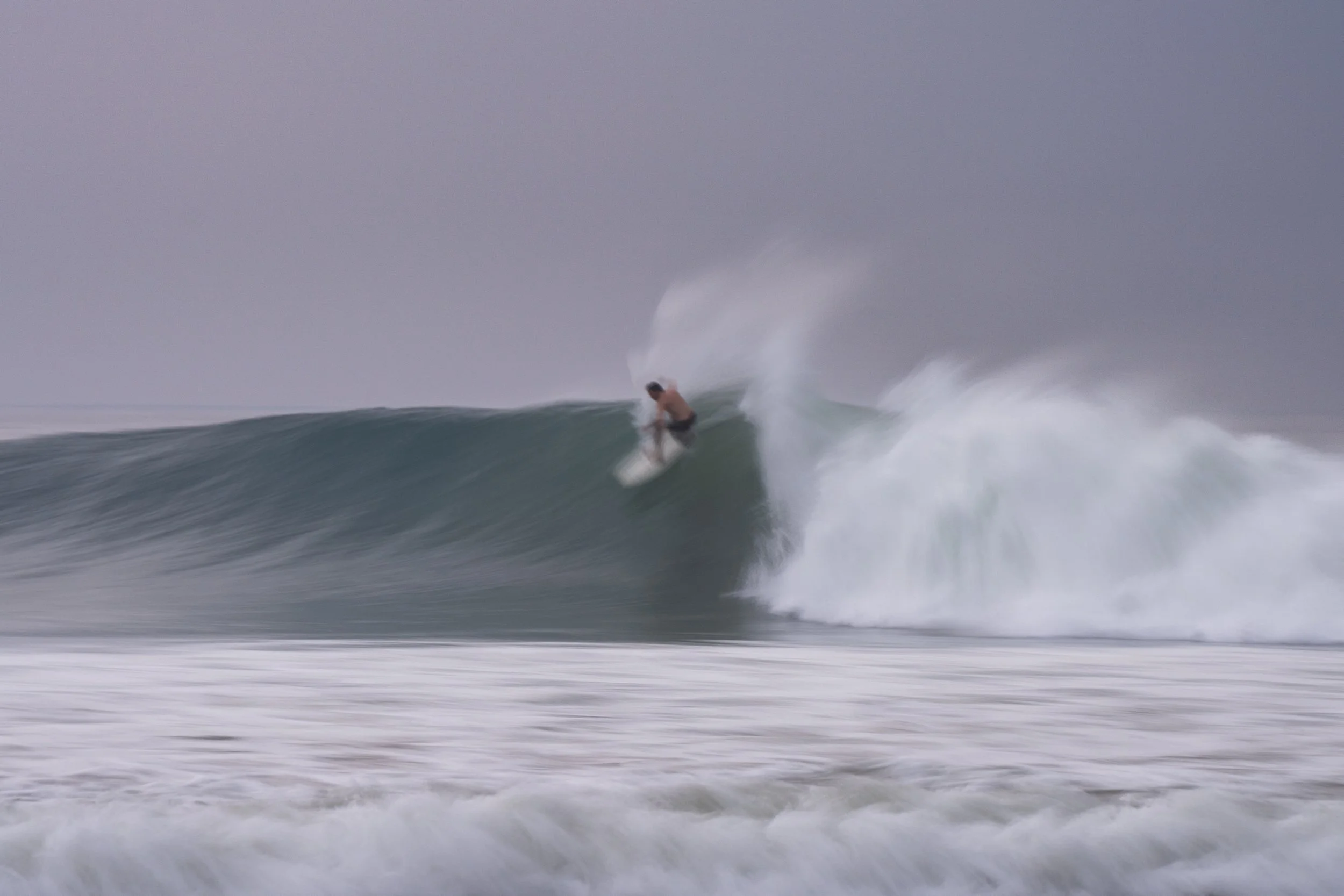 A person riding a wave on a surfboard in the ocean on a cloudy day.