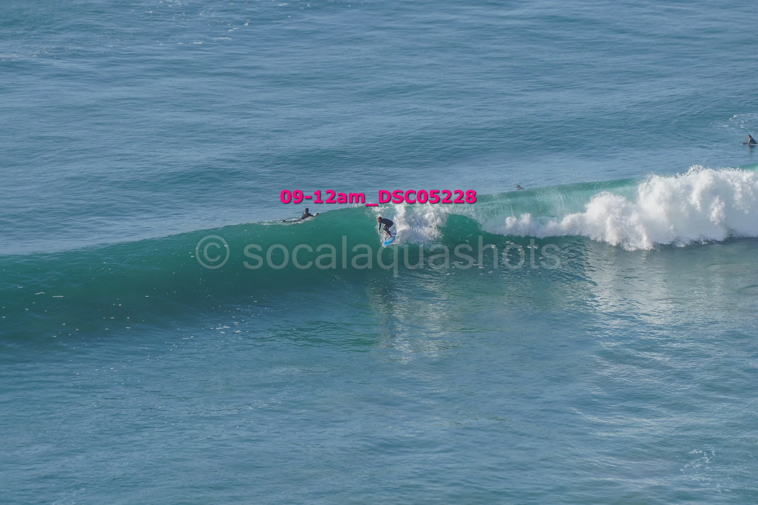 A person surfing on a wave with several other surfers in the water, ocean scene during daytime.
