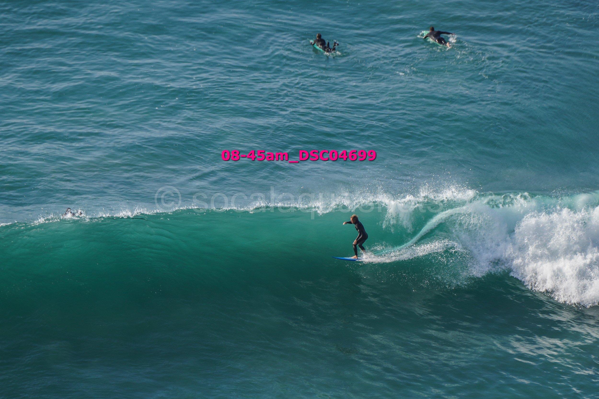 A person surfing on a wave with two swimmers in the background in the ocean.