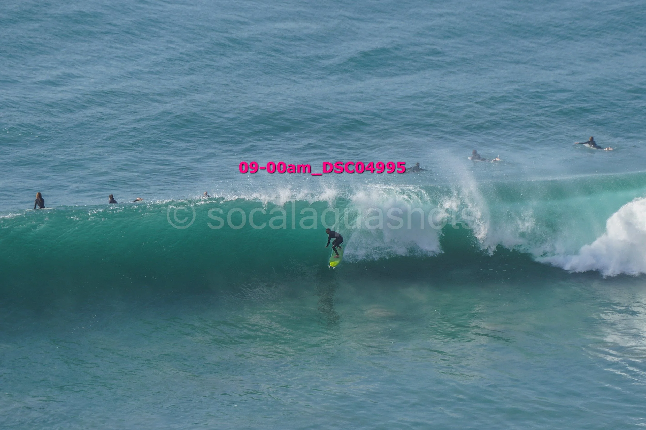 A person surfing on a large wave in the ocean with several other surfers in the background.