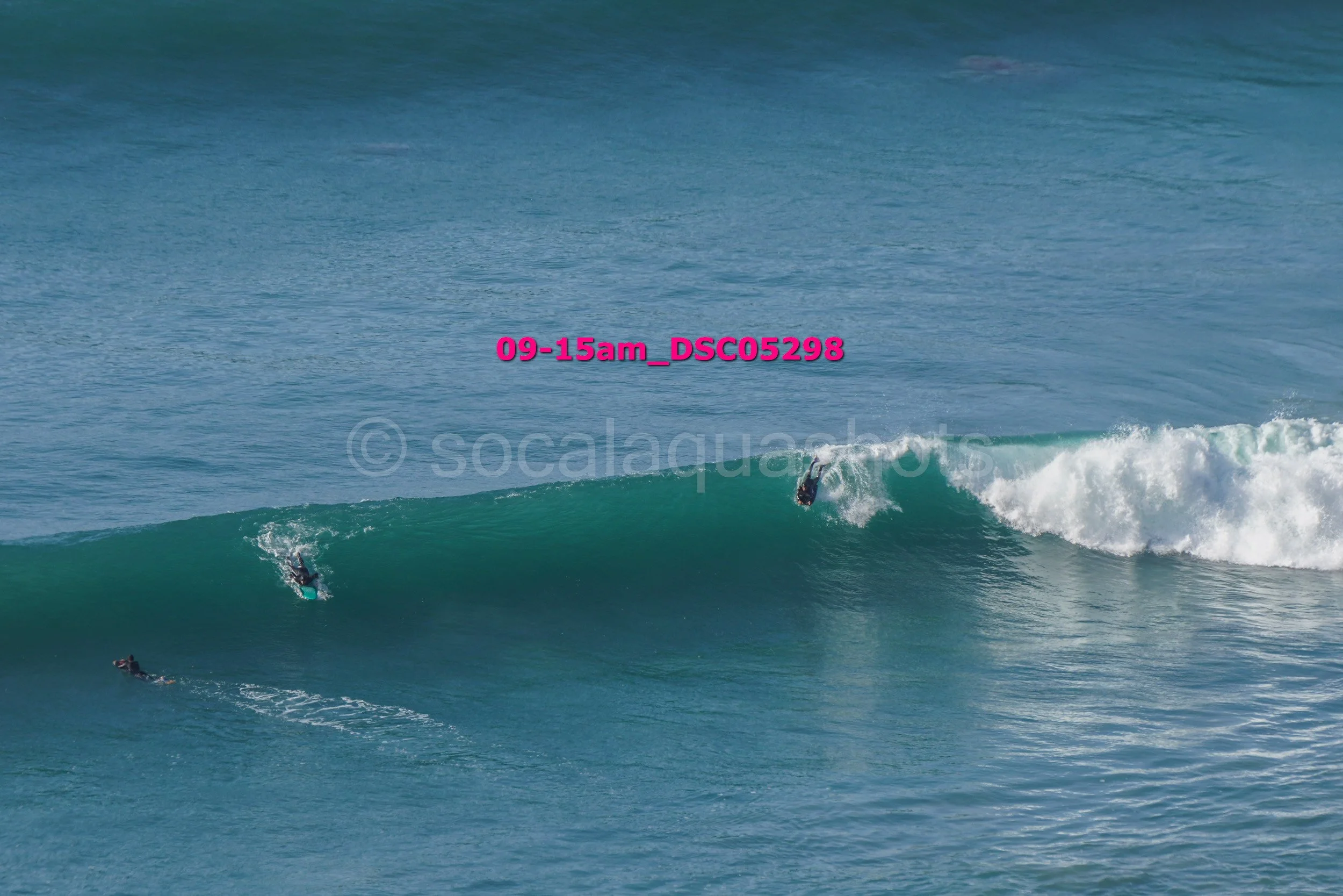Two surfers riding a large wave in the ocean, with a third surfer paddling nearby.