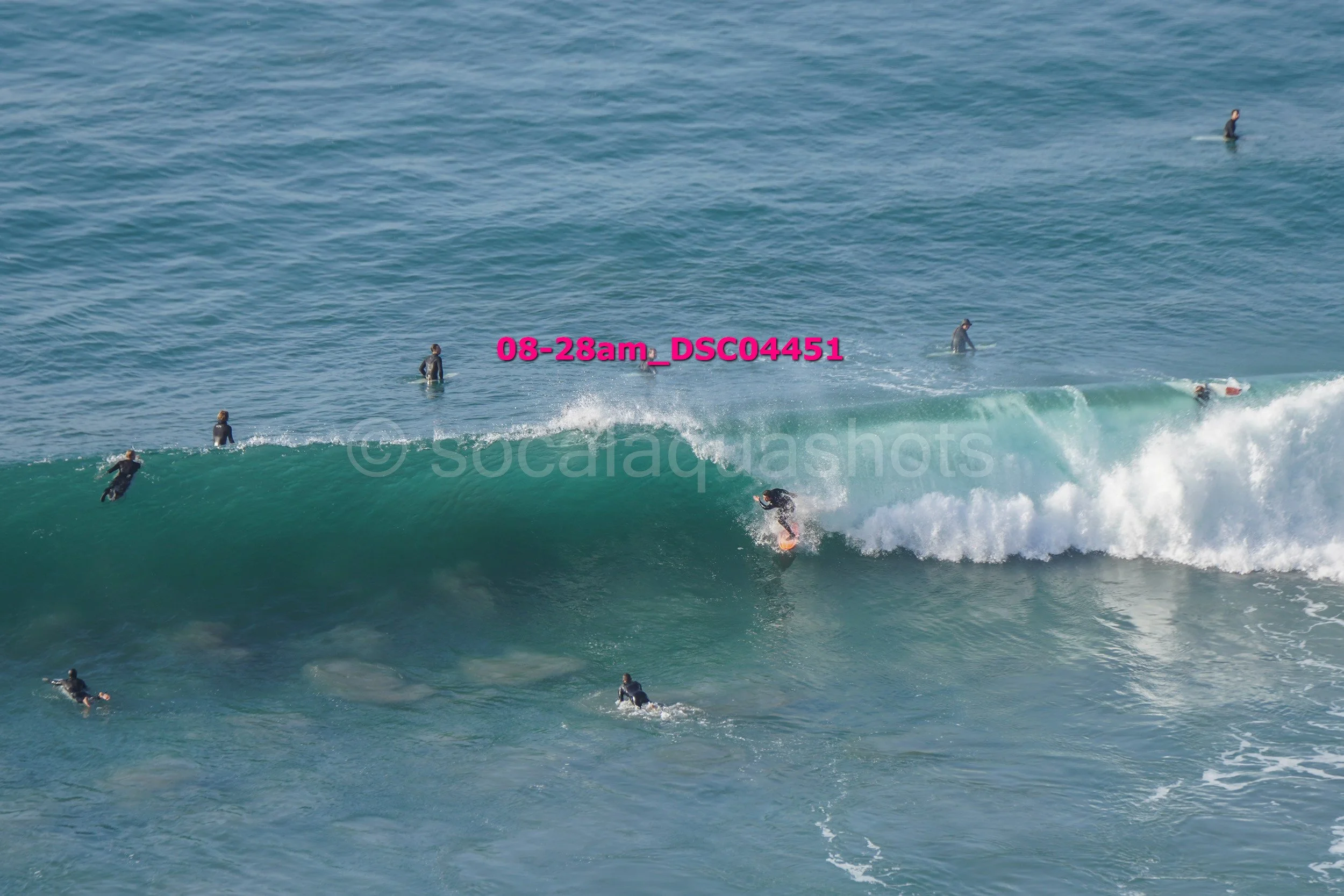 Surfer riding a large wave with several surfers in the water around him in the ocean.