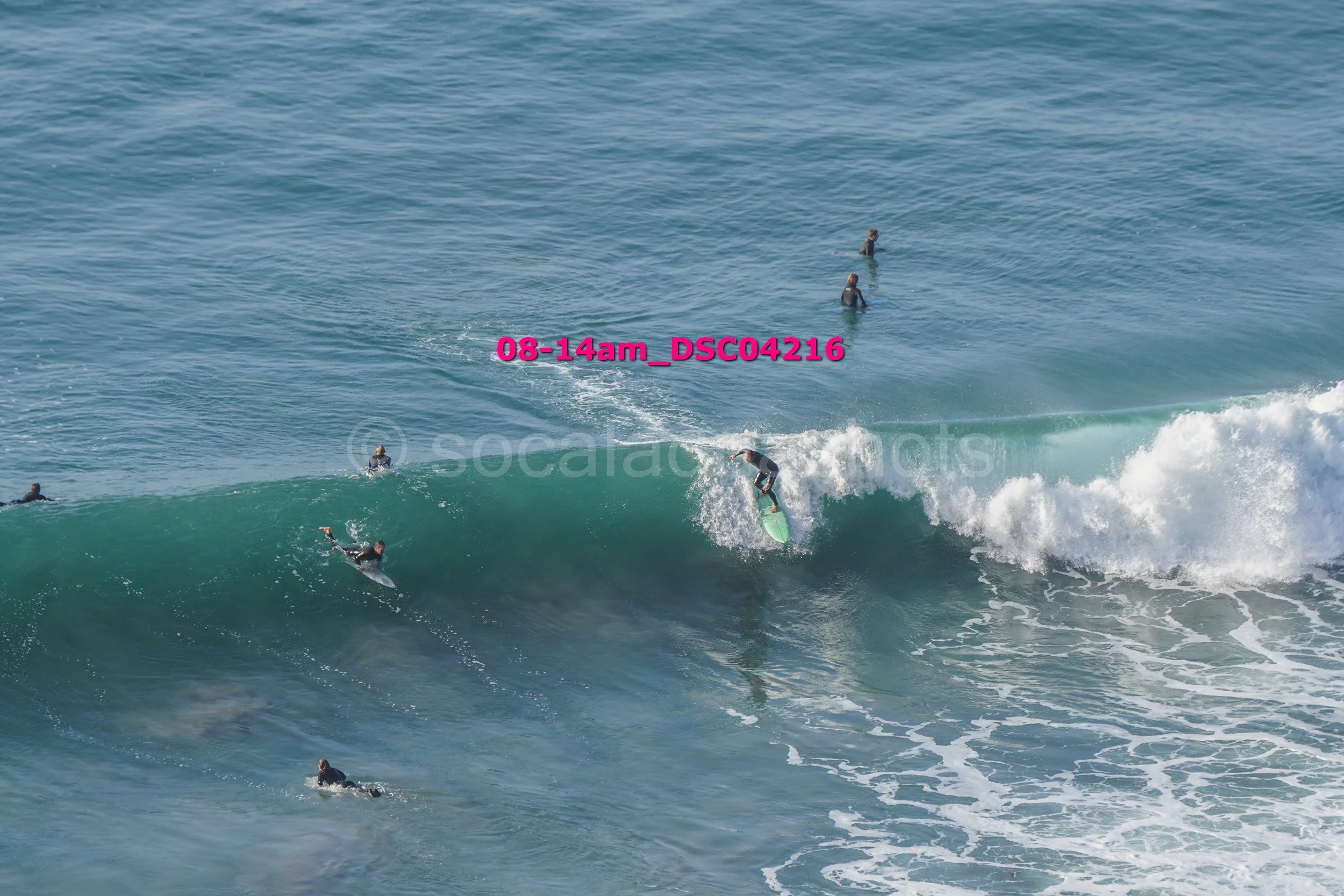 Surfer riding a wave with several people in the water watching from different positions.