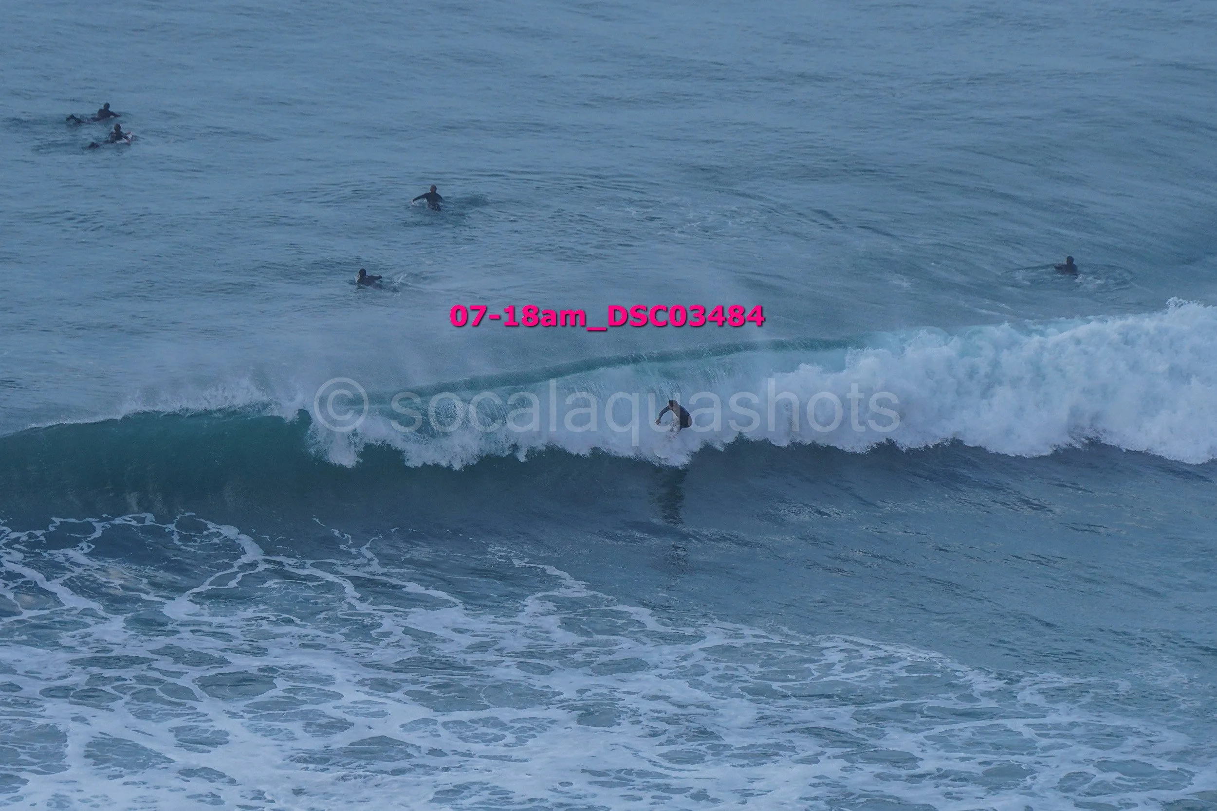 Surfer riding a wave in the ocean surrounded by several other surfers waiting in the water.