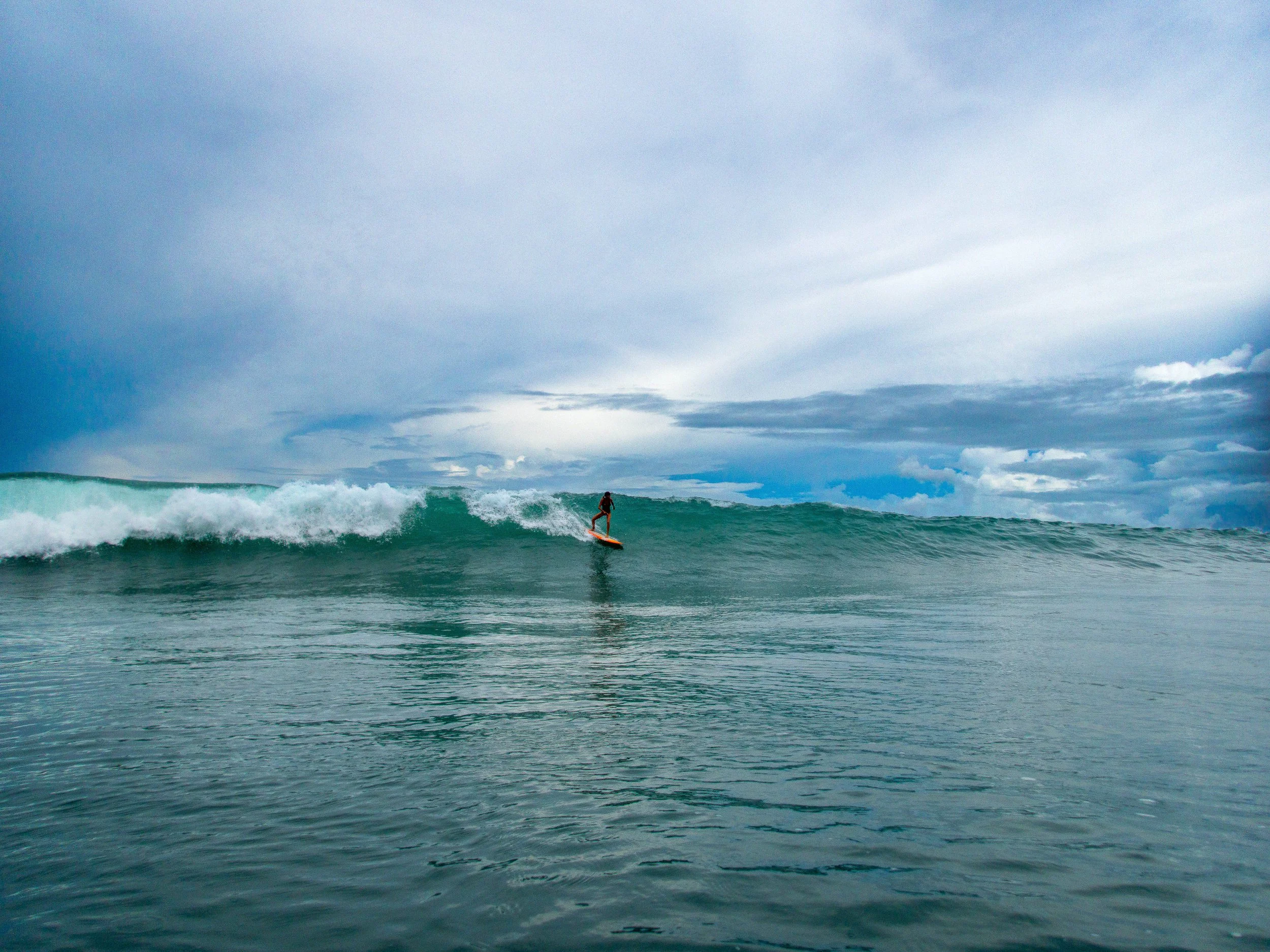Surfer riding a wave under cloudy sky