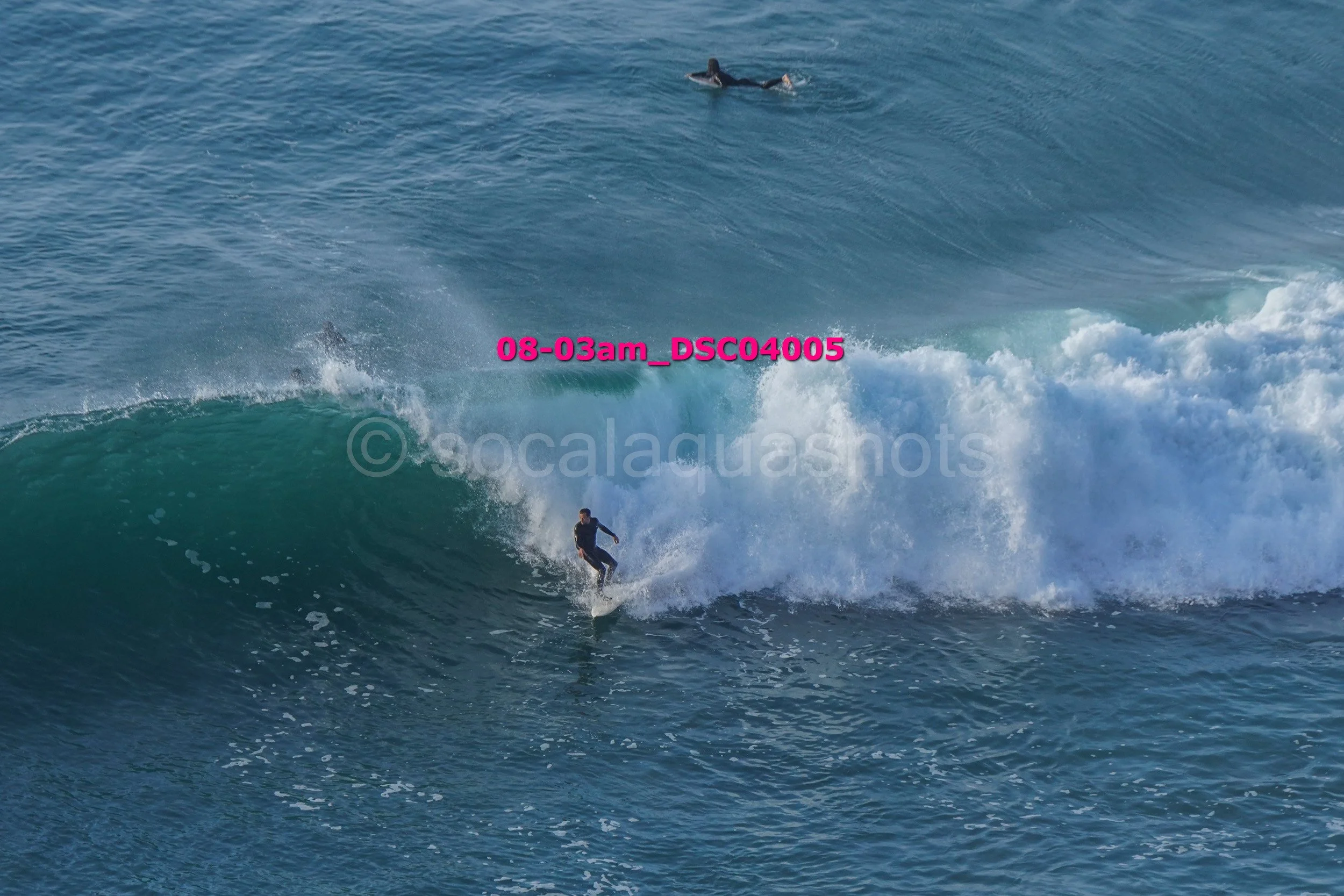 Surfer riding a large wave in the ocean with another swimmer in the background.