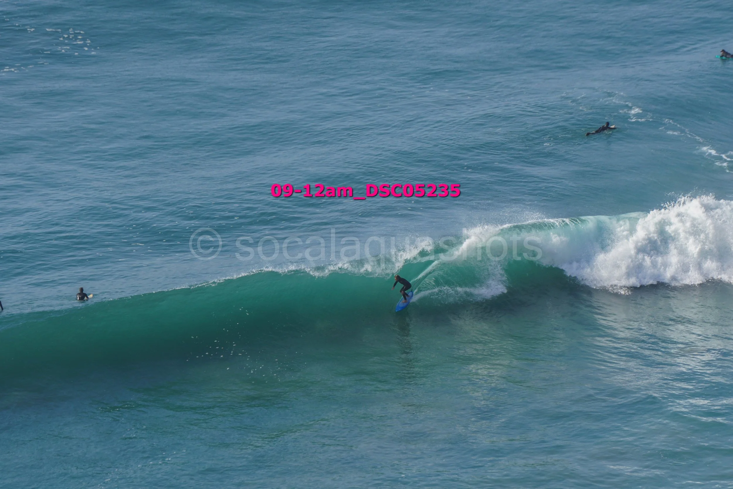 Surfer riding a wave with several other surfers in the water.