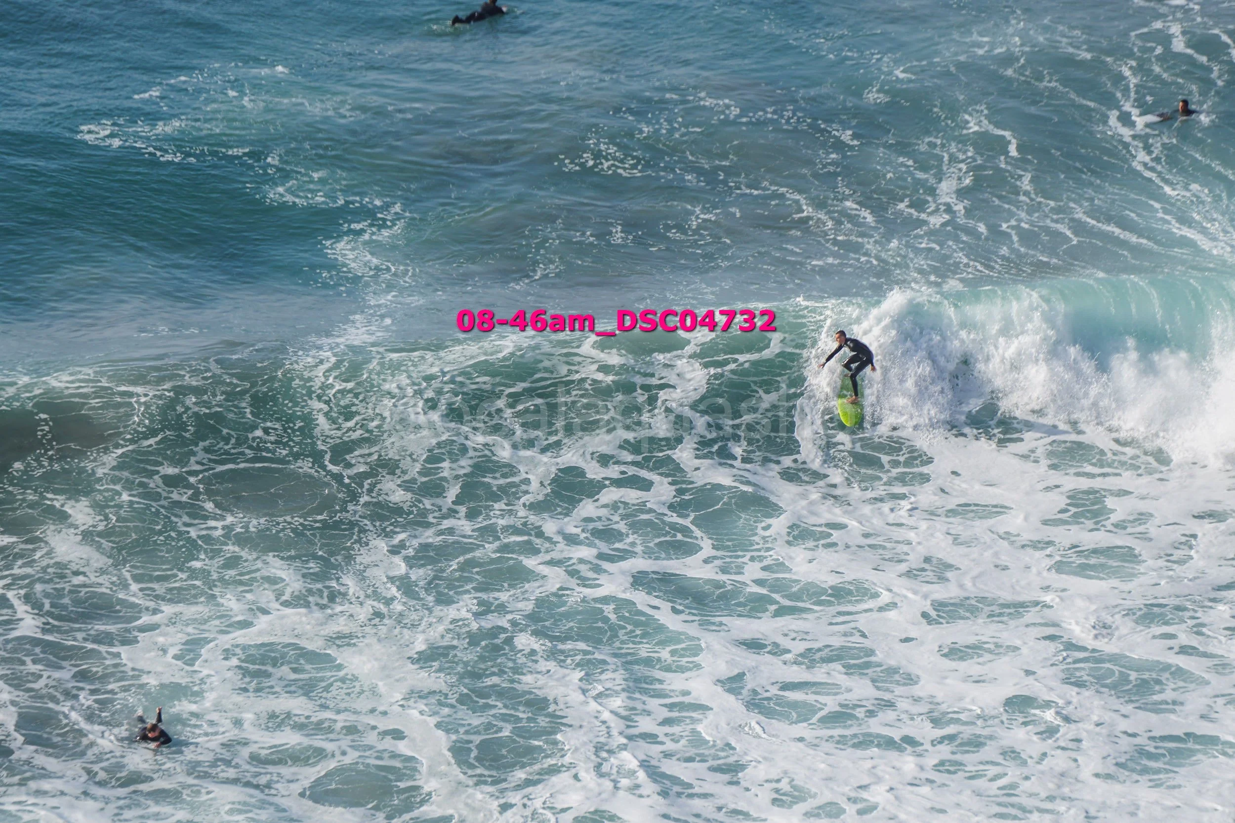 A person surfing on a wave in the ocean, with other surfers visible in the water.