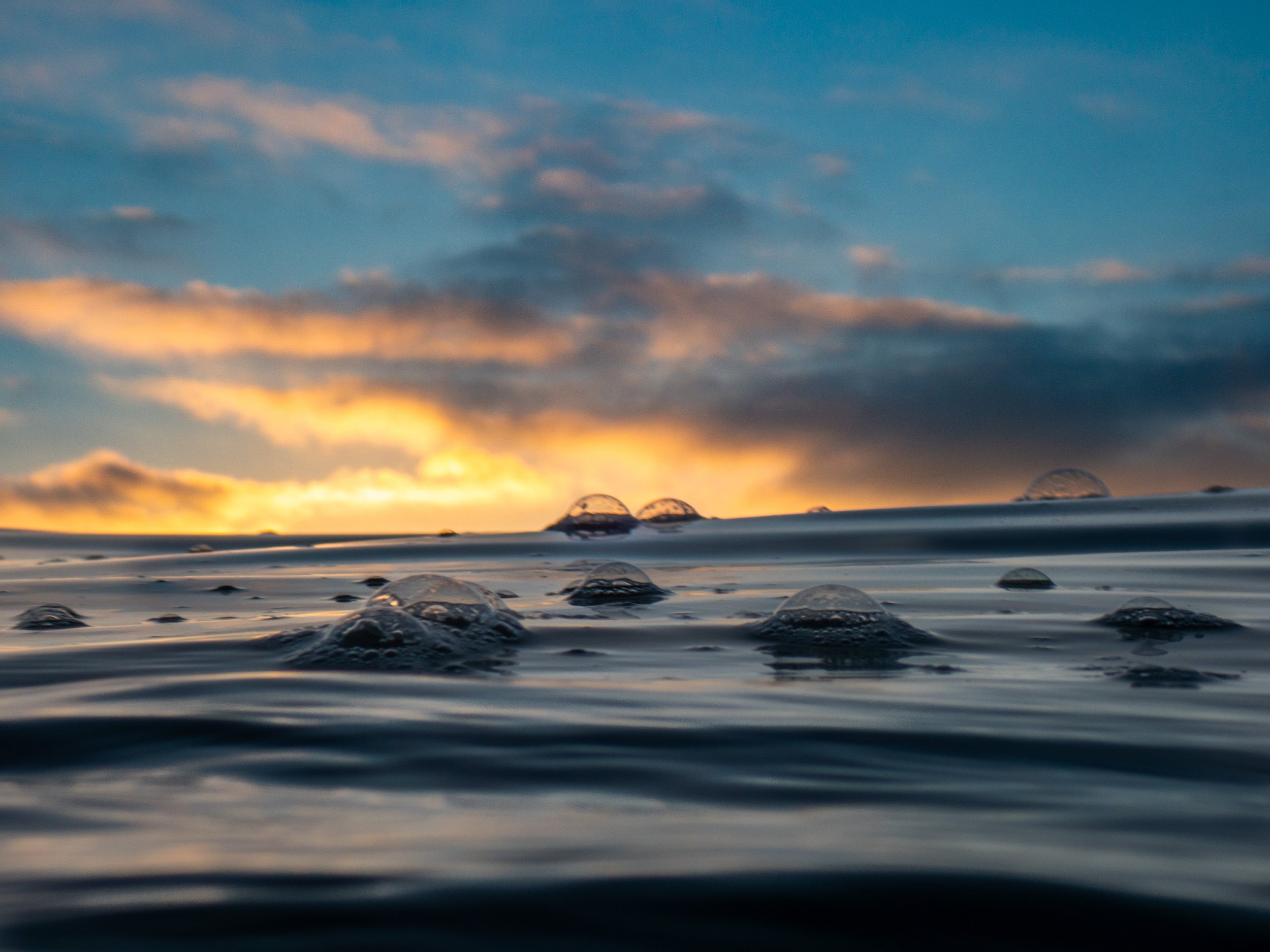 Close-up view of ocean water with small bubbles and ripples during sunset with colorful sky and clouds