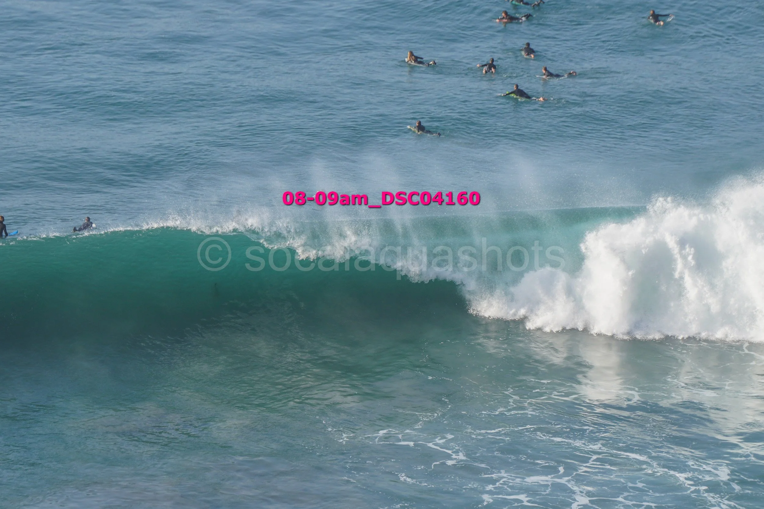 A group of surfers waiting in the water to ride a large wave near the shoreline.