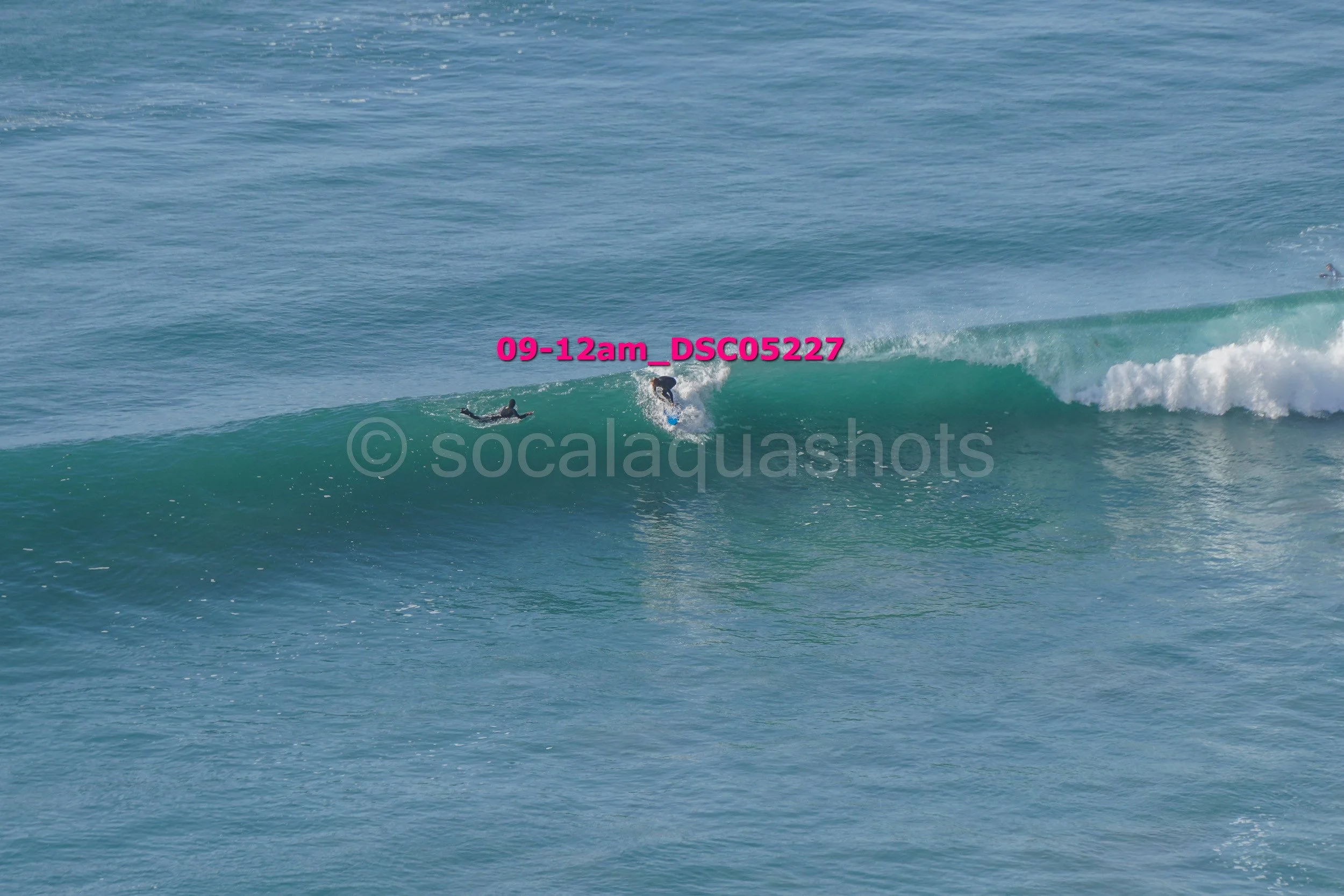 Surfer riding a wave in the ocean, with another surfer lying on the water nearby.