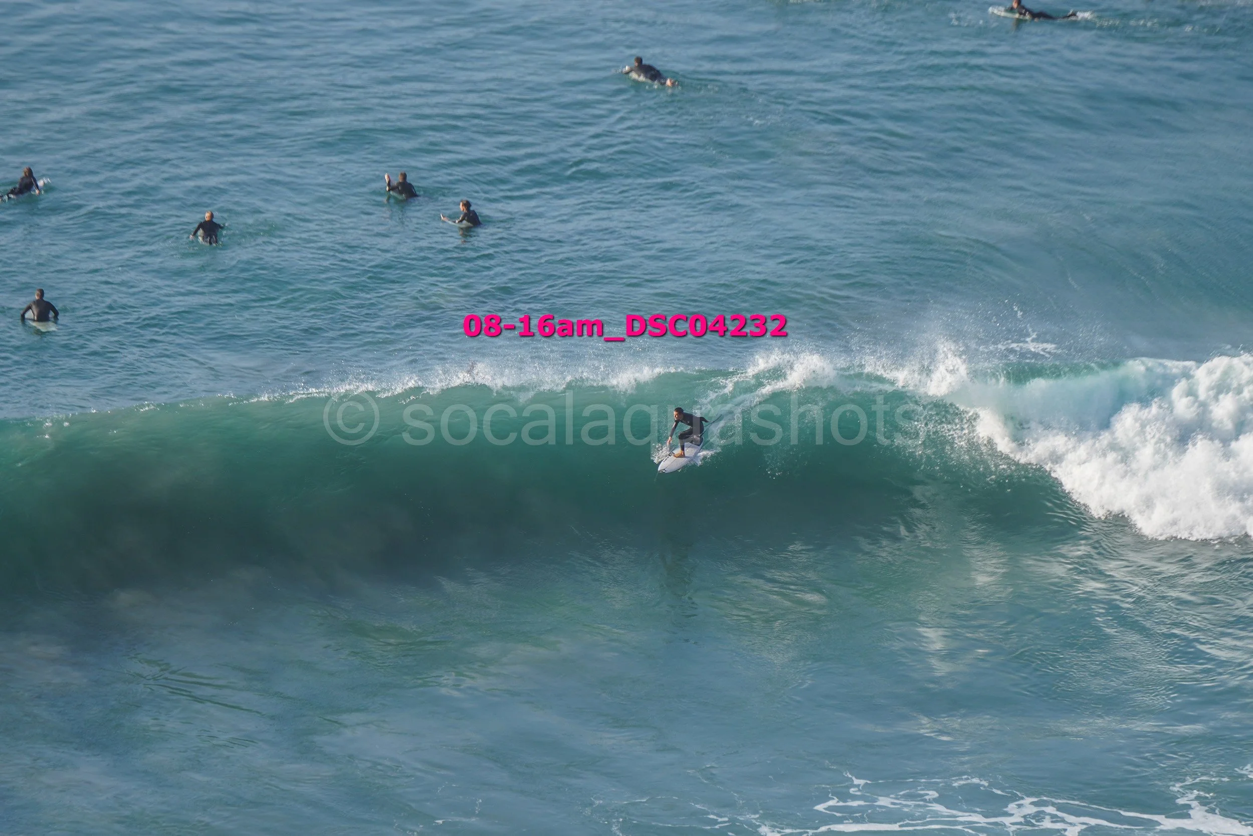 A person surfing on a wave with multiple surfers in the ocean around them.