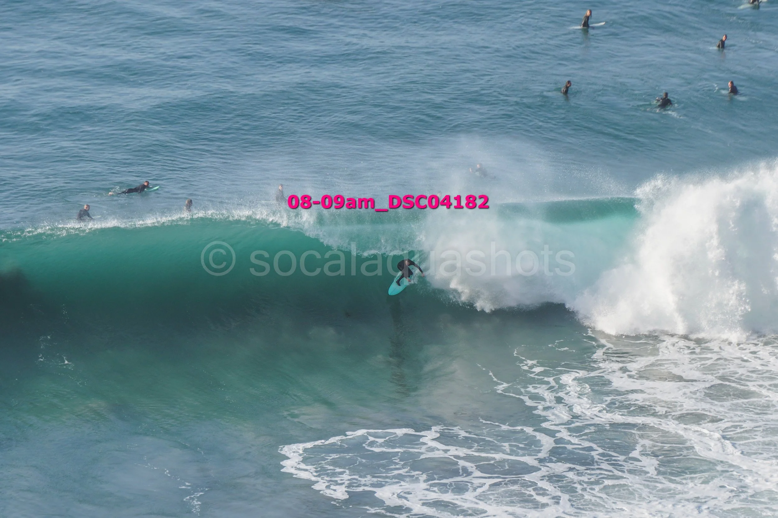 A surfer riding a wave with several other surfers in the water nearby.
