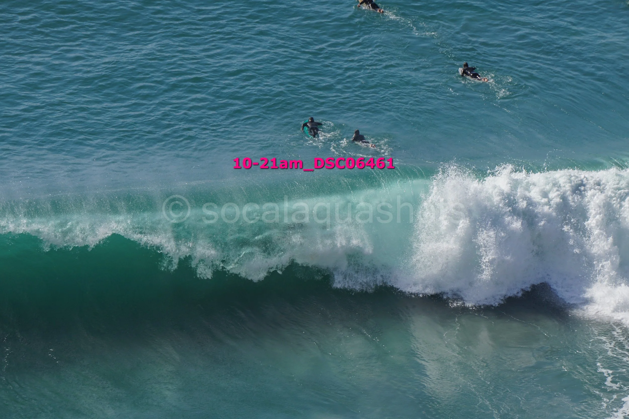 Three surfers paddling in the ocean with large waves breaking nearby.