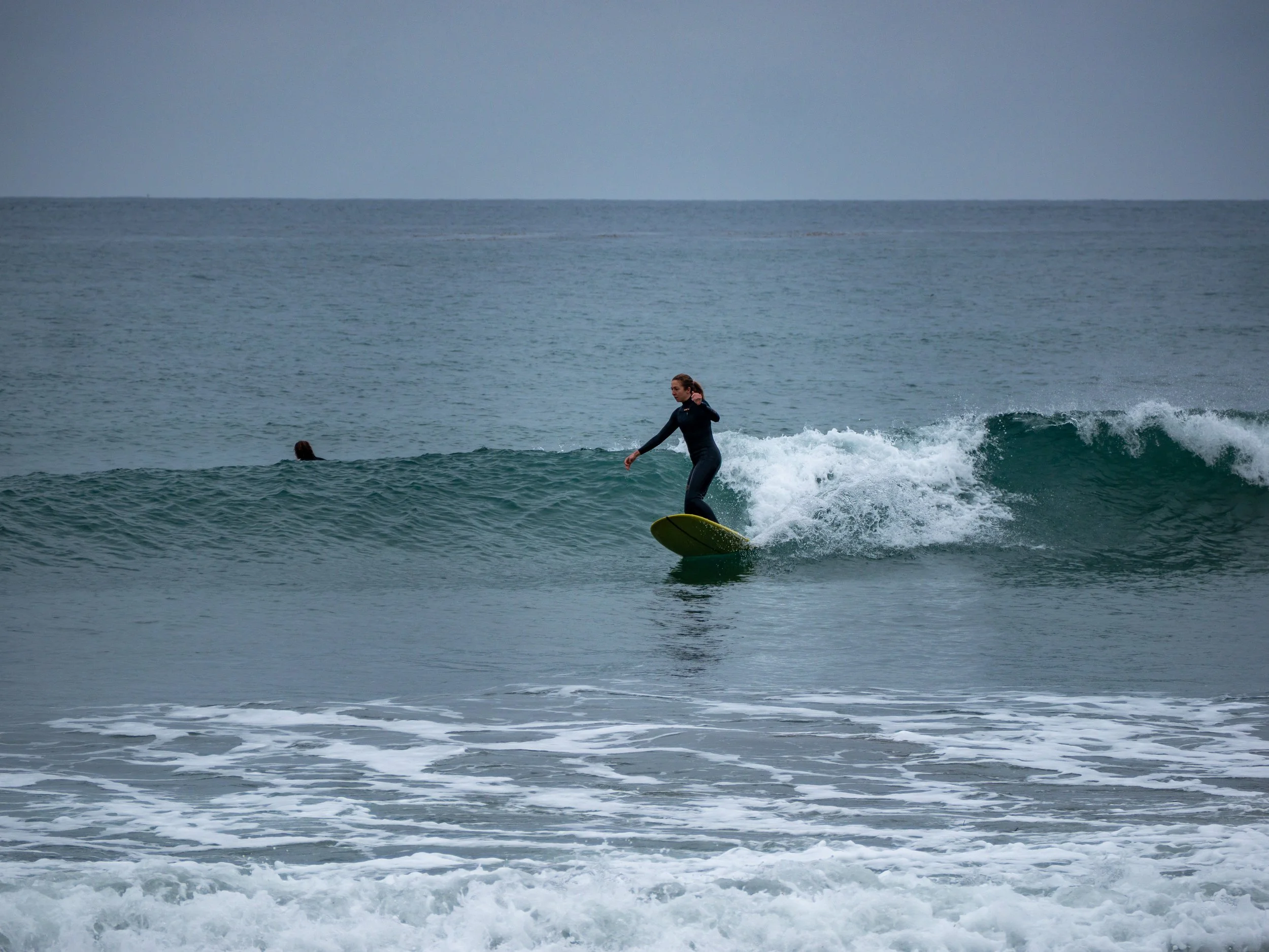 A woman surfing on a small wave in the ocean during daytime, wearing a wetsuit and balancing on a surfboard.