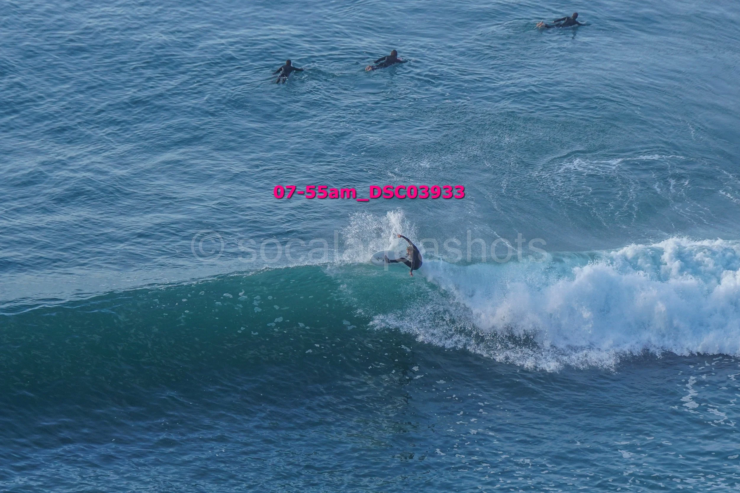 A person surfing on a wave in the ocean, with three other people floating in the water nearby