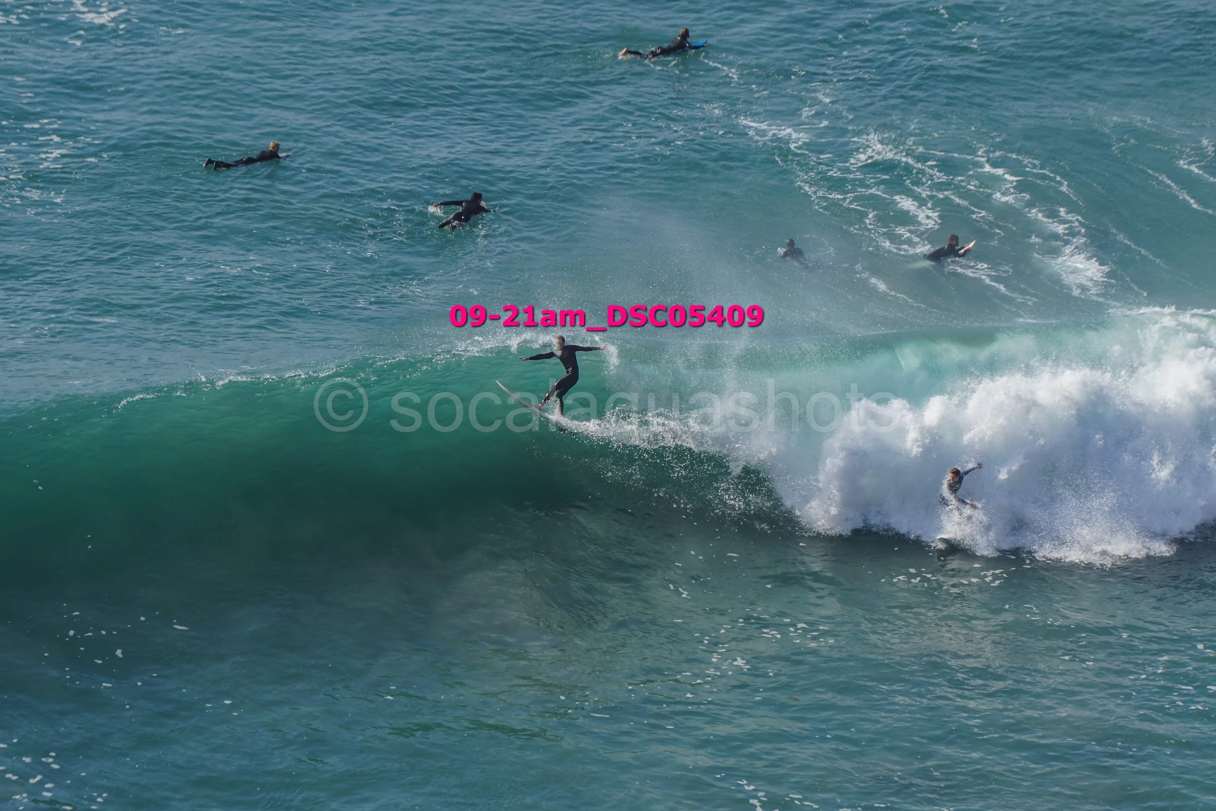 Surfer riding a large wave with multiple surfers in the water behind them.
